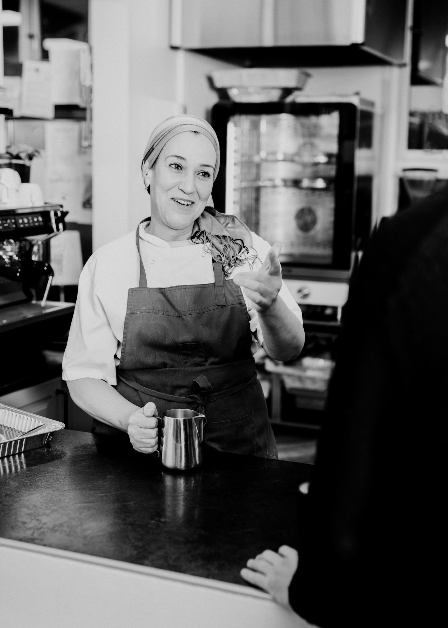 Foto av Nayat Abbouz som betjener en kunde på Kulturkafeen bak kassen med et smil om munnen