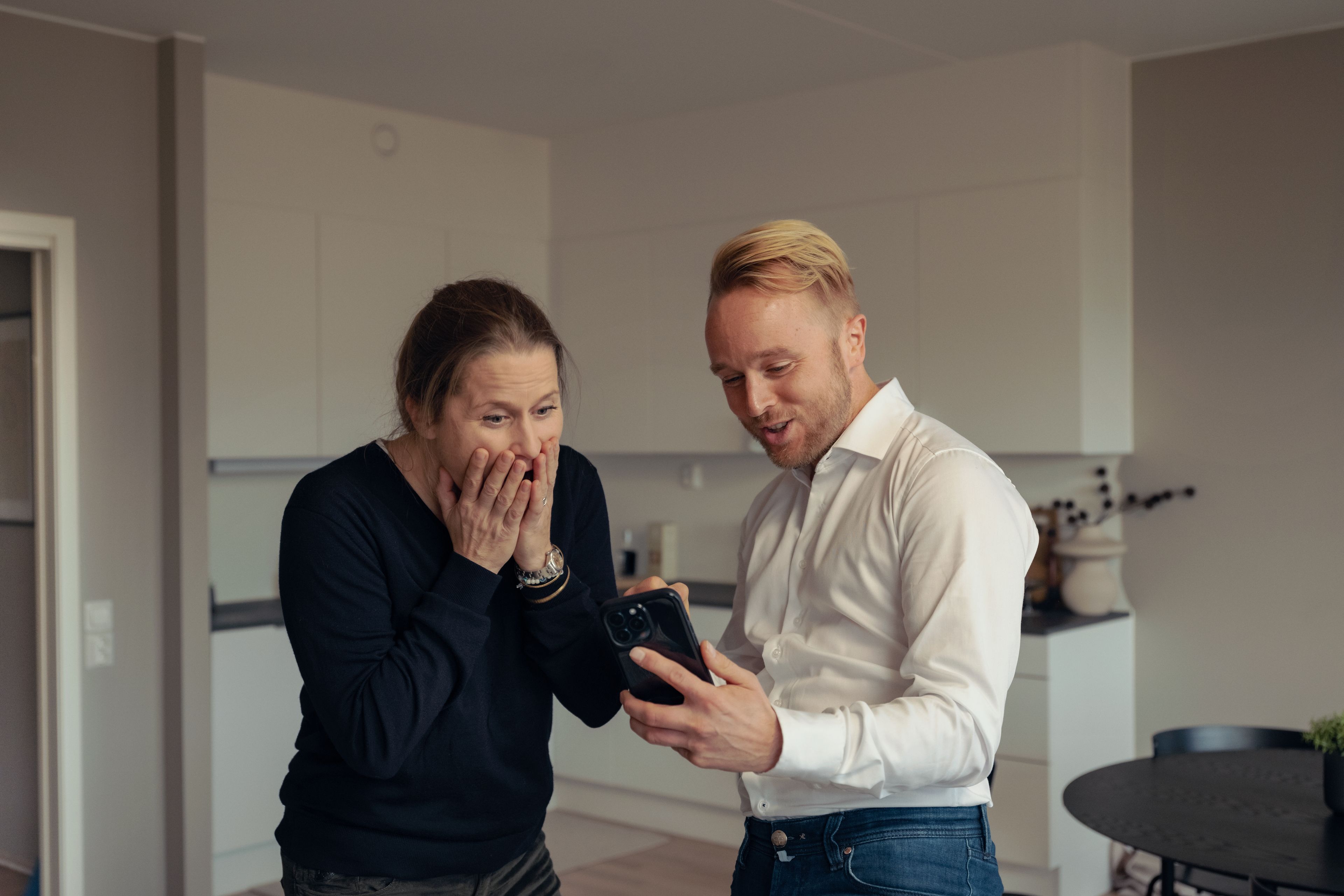 En dame og en mann ser på en mobiltelefon og er glade, overraskede og fornøyde.