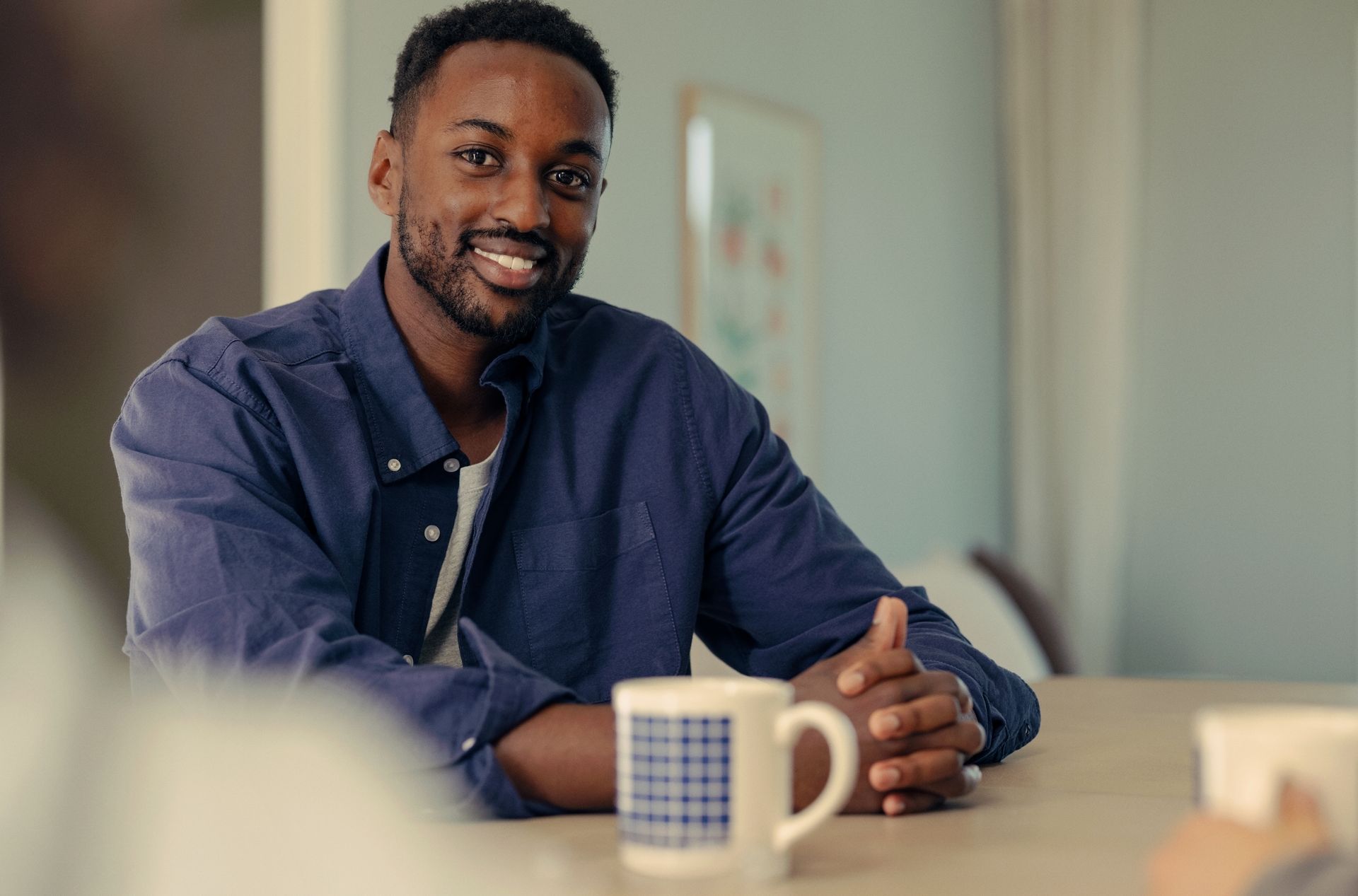 Mann sitter med en kaffekopp ved et bord og ser mot kamera