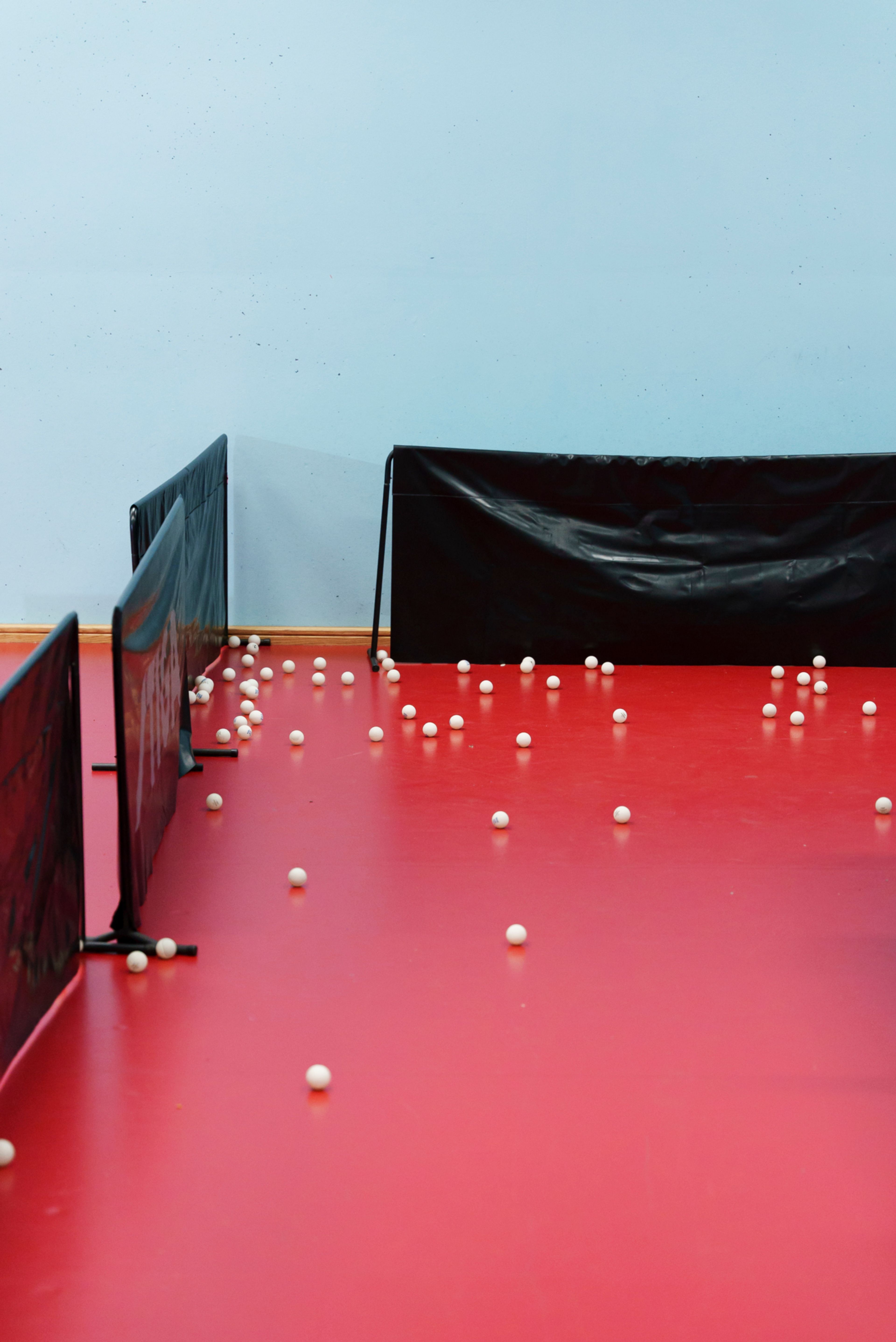 Flere titalls bordtennisballer ligger strødd utover gulvet etter trening.