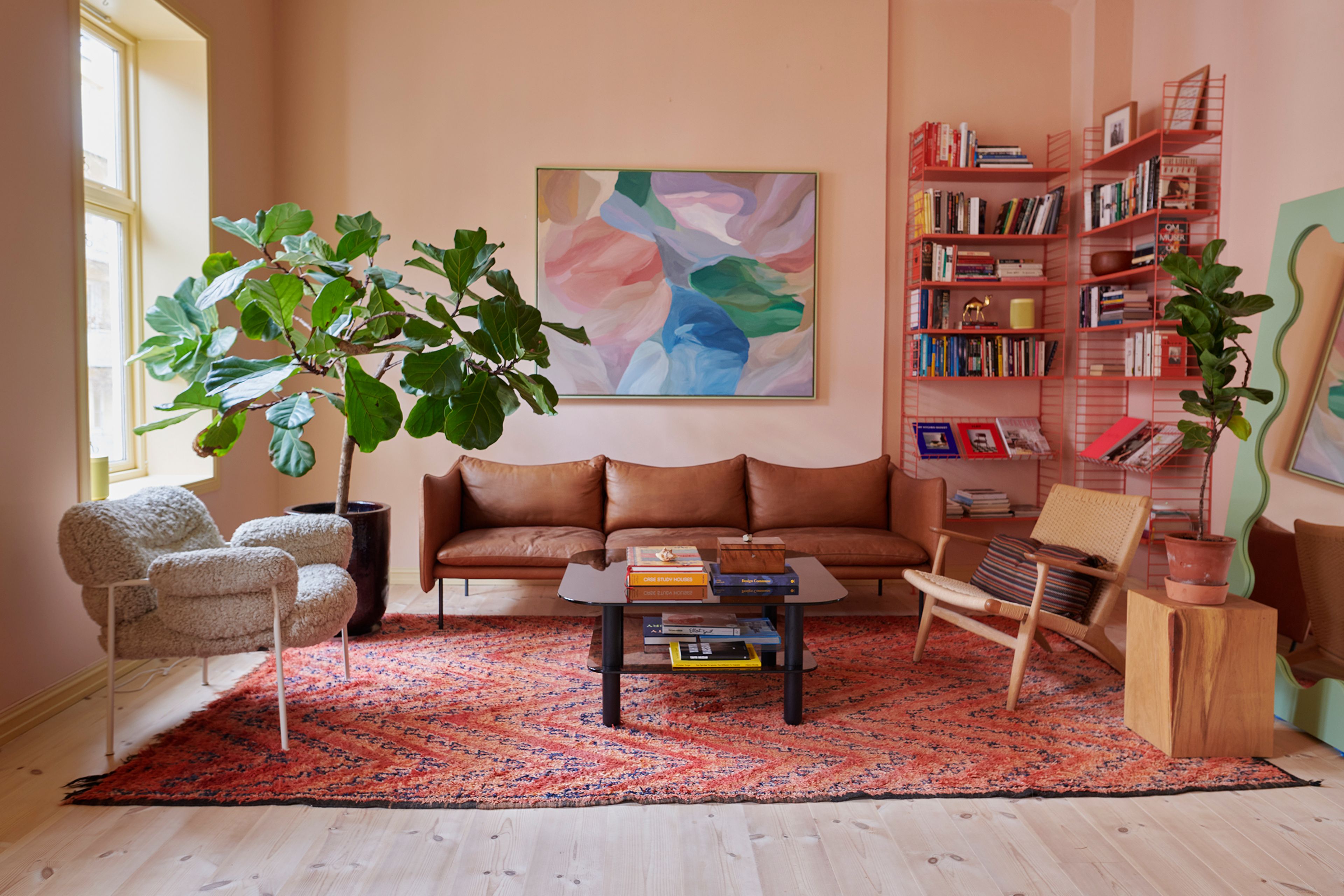 Stue med sofa, stoler, bokhylle, fikentre og vegger malt i en dus, rosa farge.