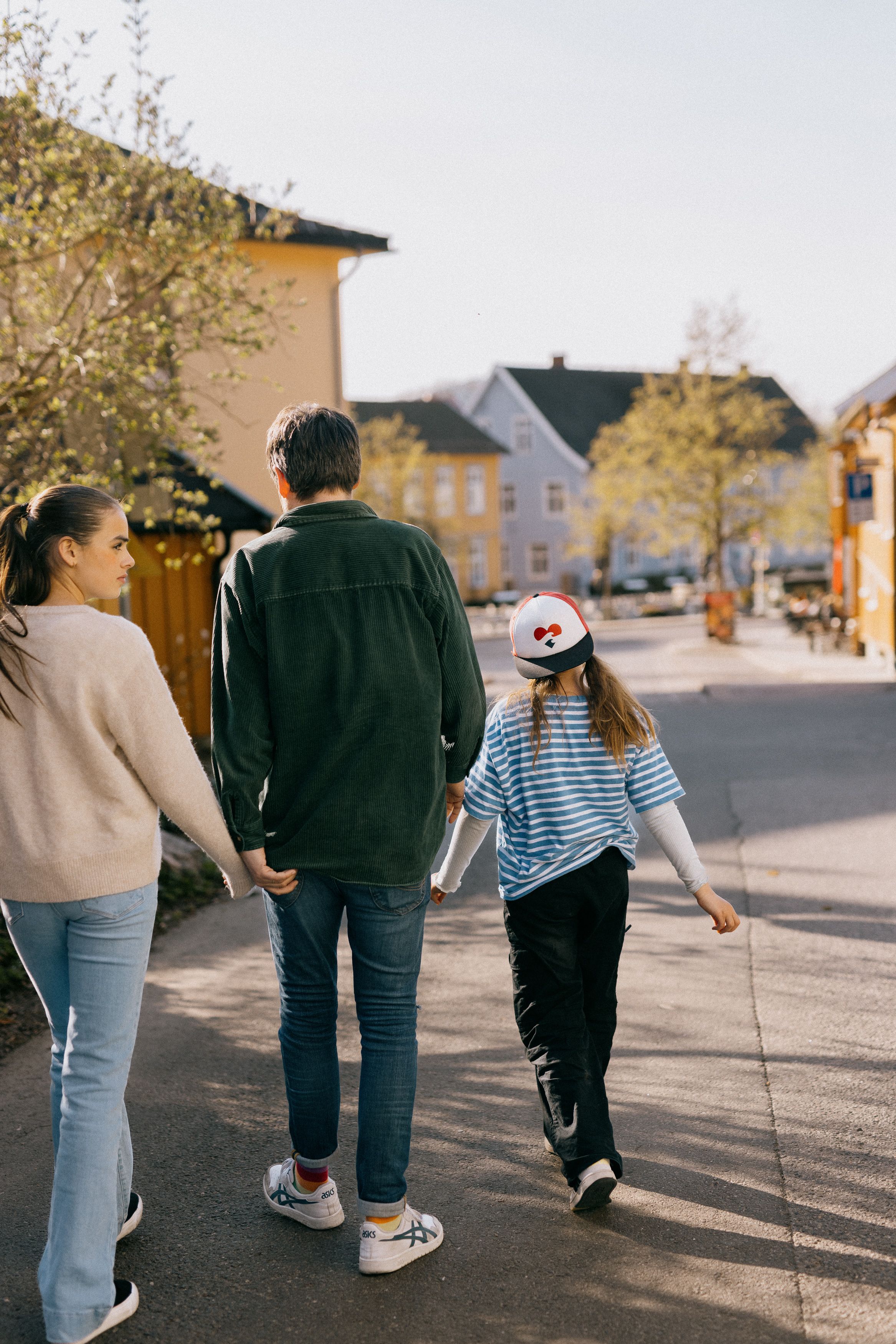En mann og to jenter går bortover. Du ser dem med ryggen til.