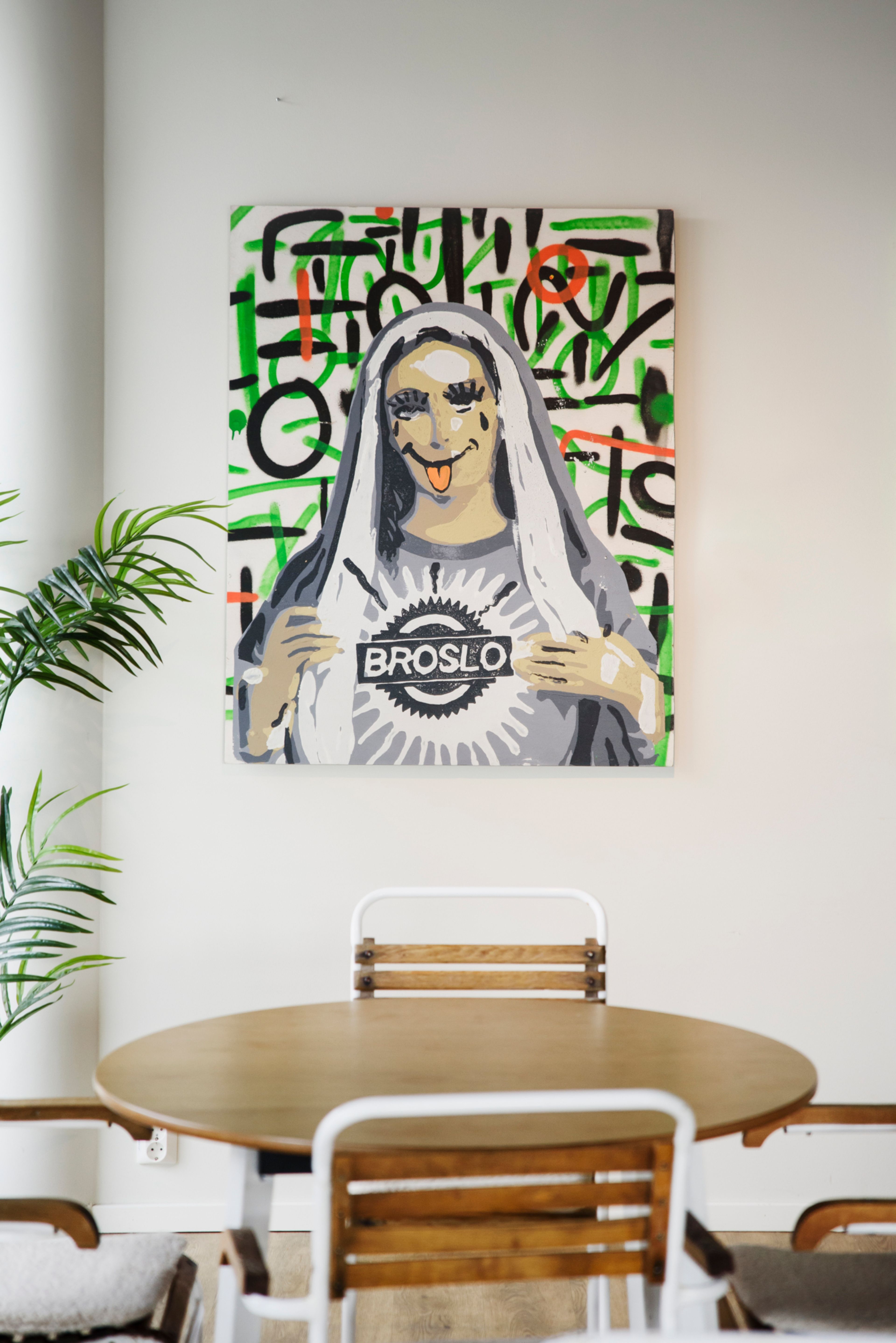 Rundt bord og fire stoler i tre foran en hvitmalt vegg med bilde av fargerik gatekunst på