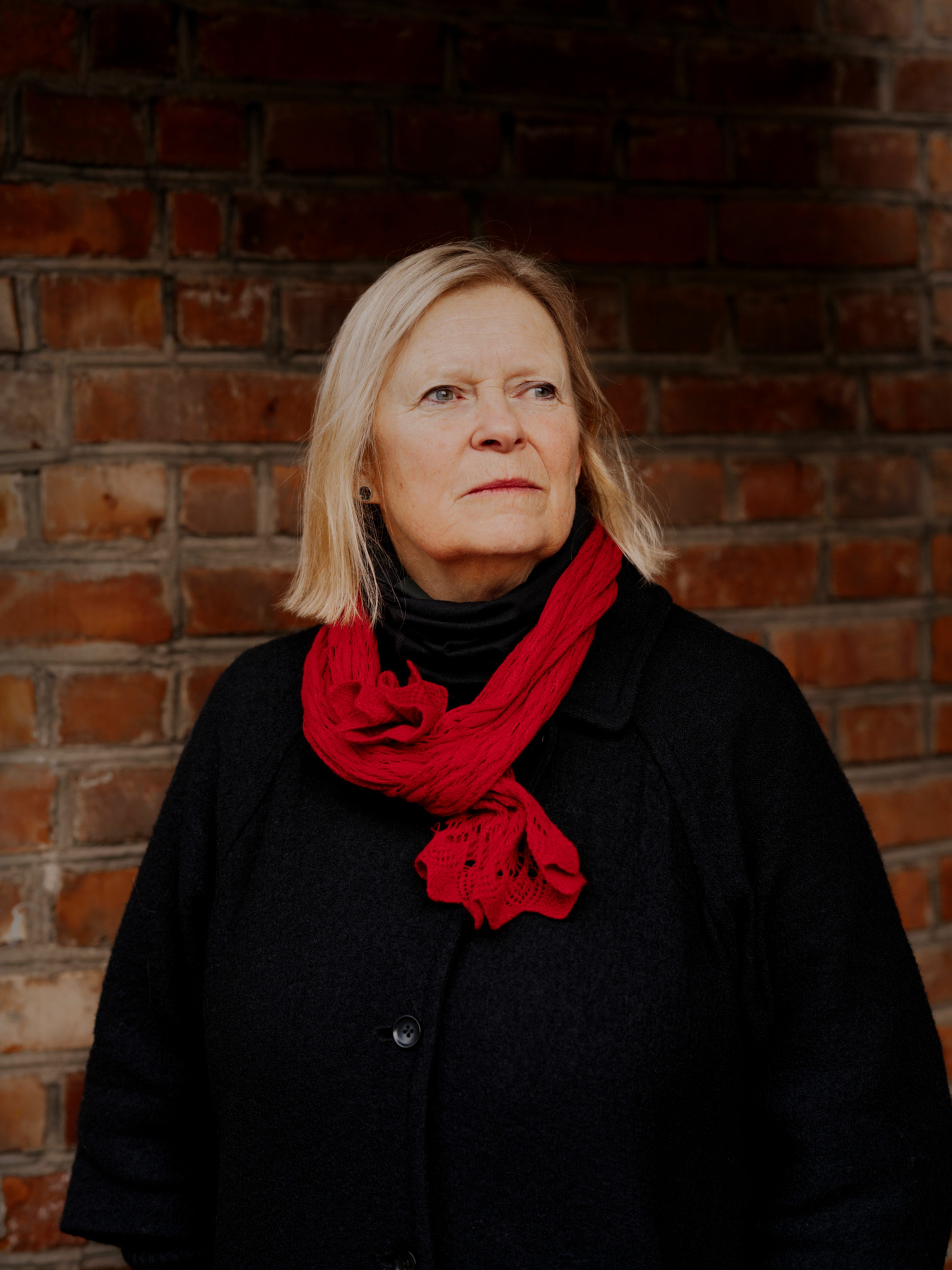 Foto av Wenche Engseth foran en murvegg. Hun har på seg et rødt skjerf og svart jakke.