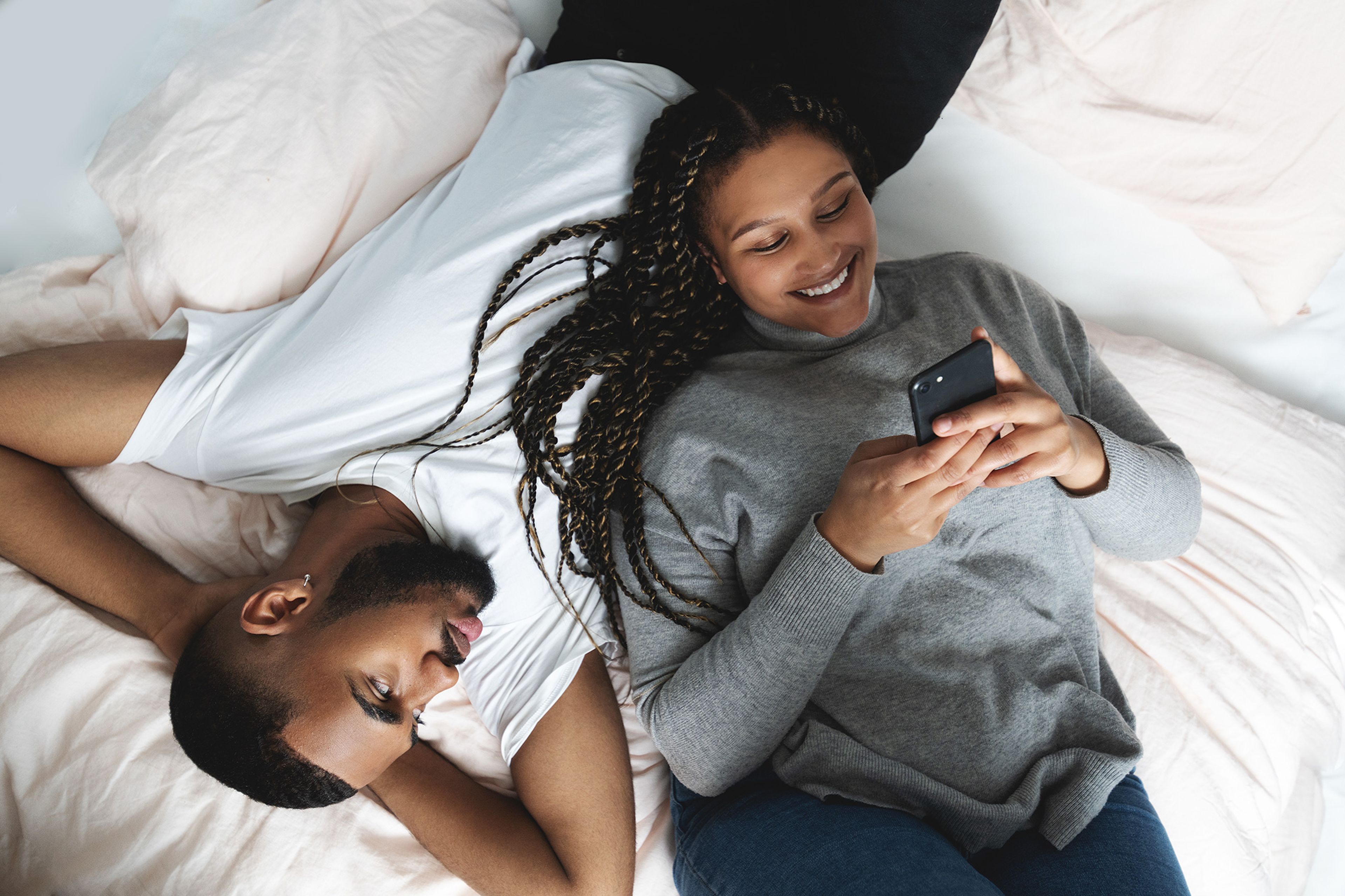 ungt part ligger i sängen och kollar på mobilen