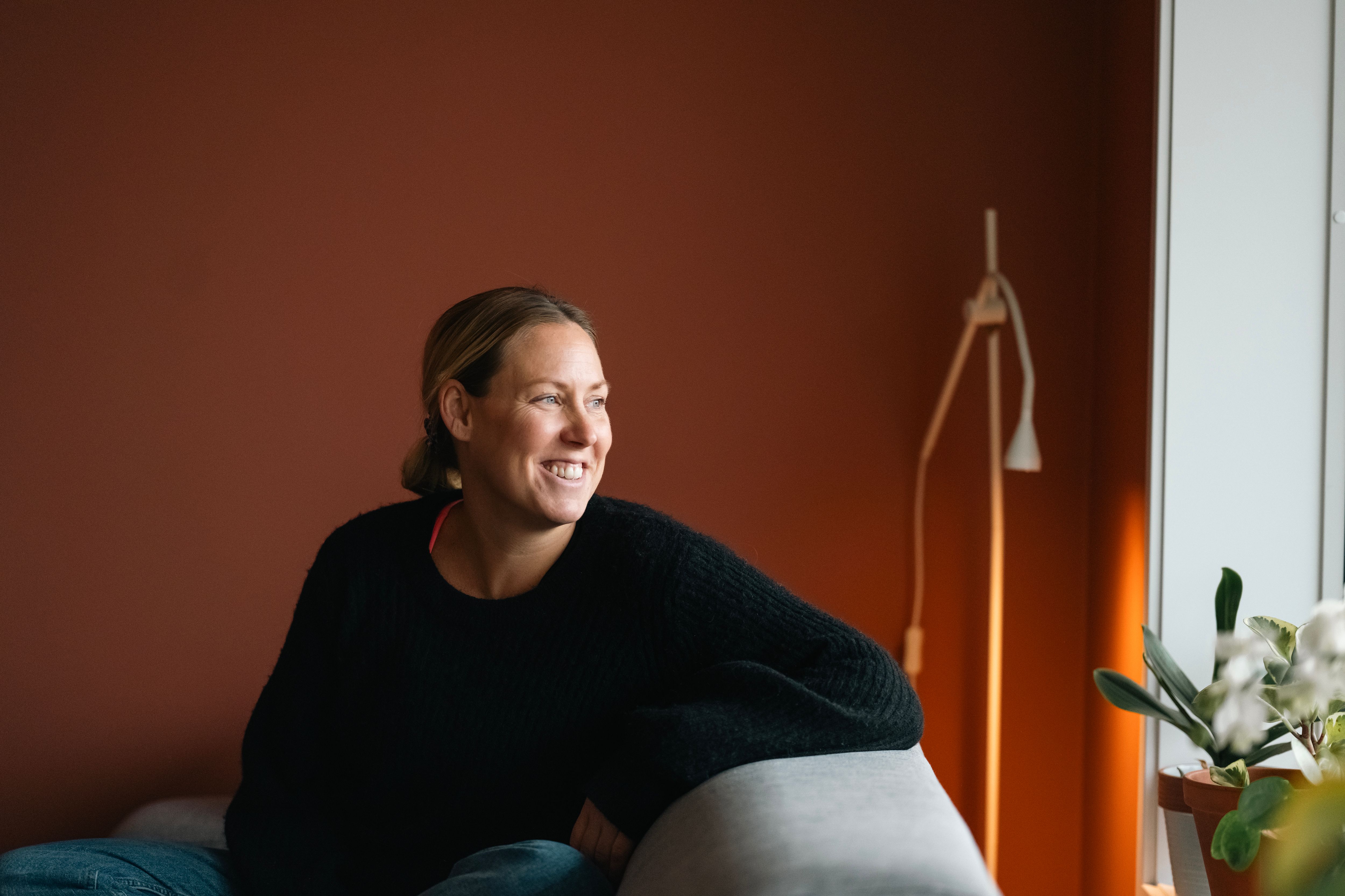 Foto av Kristin som kikker ut av vinduet i stua, i leiligheten sin på Vollebekk i Oslo