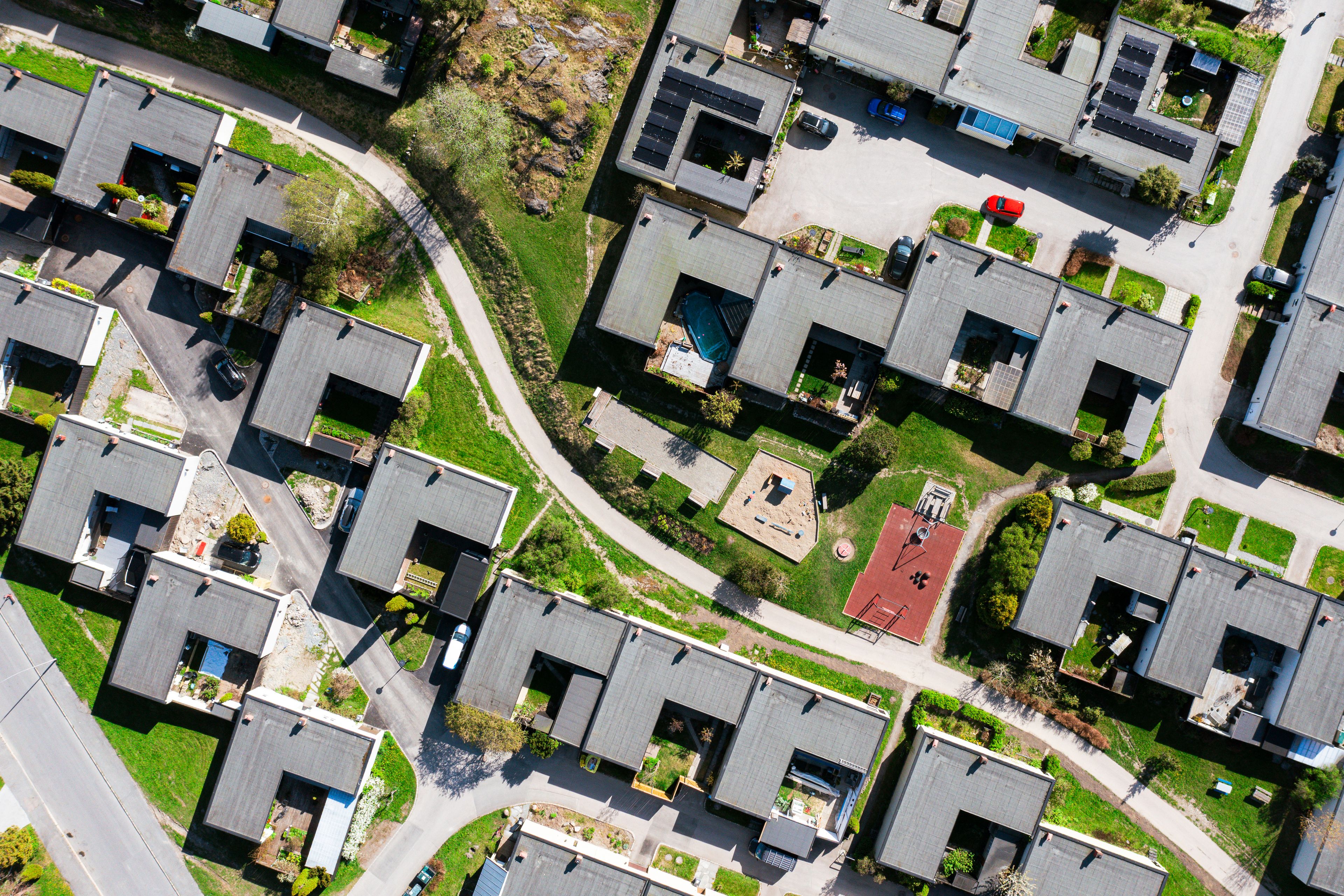 Dronefoto av et boligområde med rekkehus, grøntarealer, lekeplass og gangveier.
