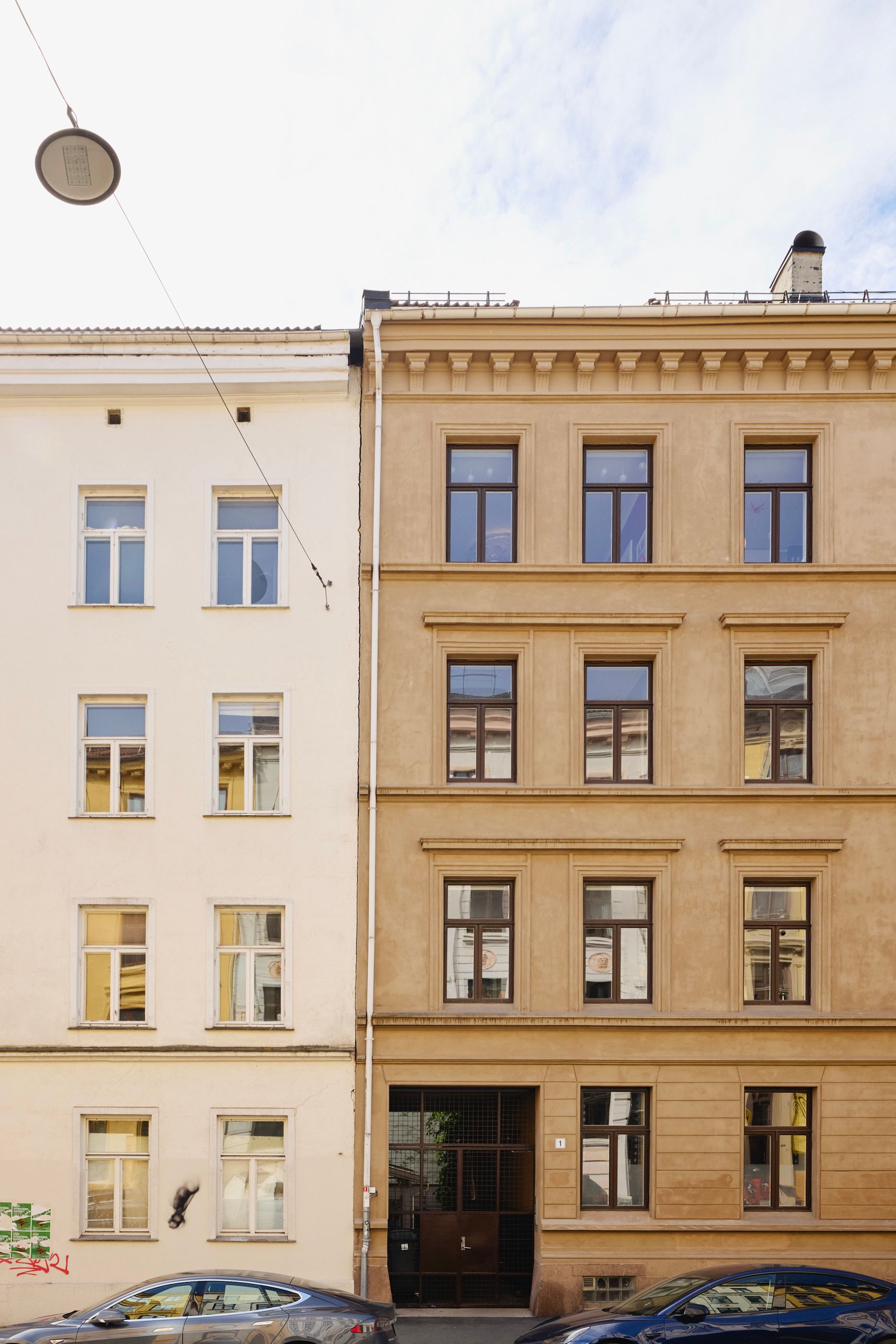En hvit og en gul bygård ved siden av hverandre. To biler står parkert i gata foran bygningene.