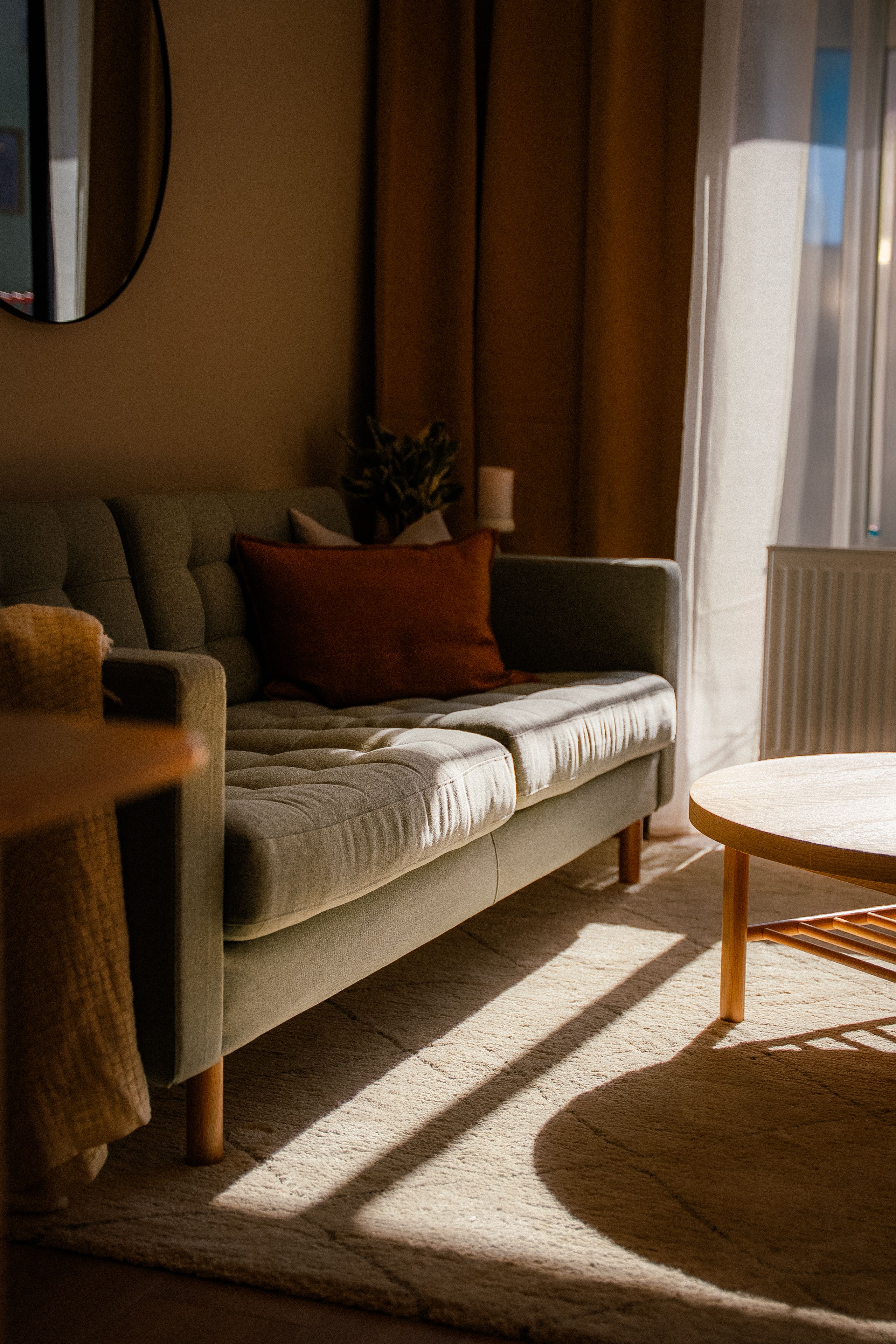 En sofa med pledd og puter i varme jordfarger.