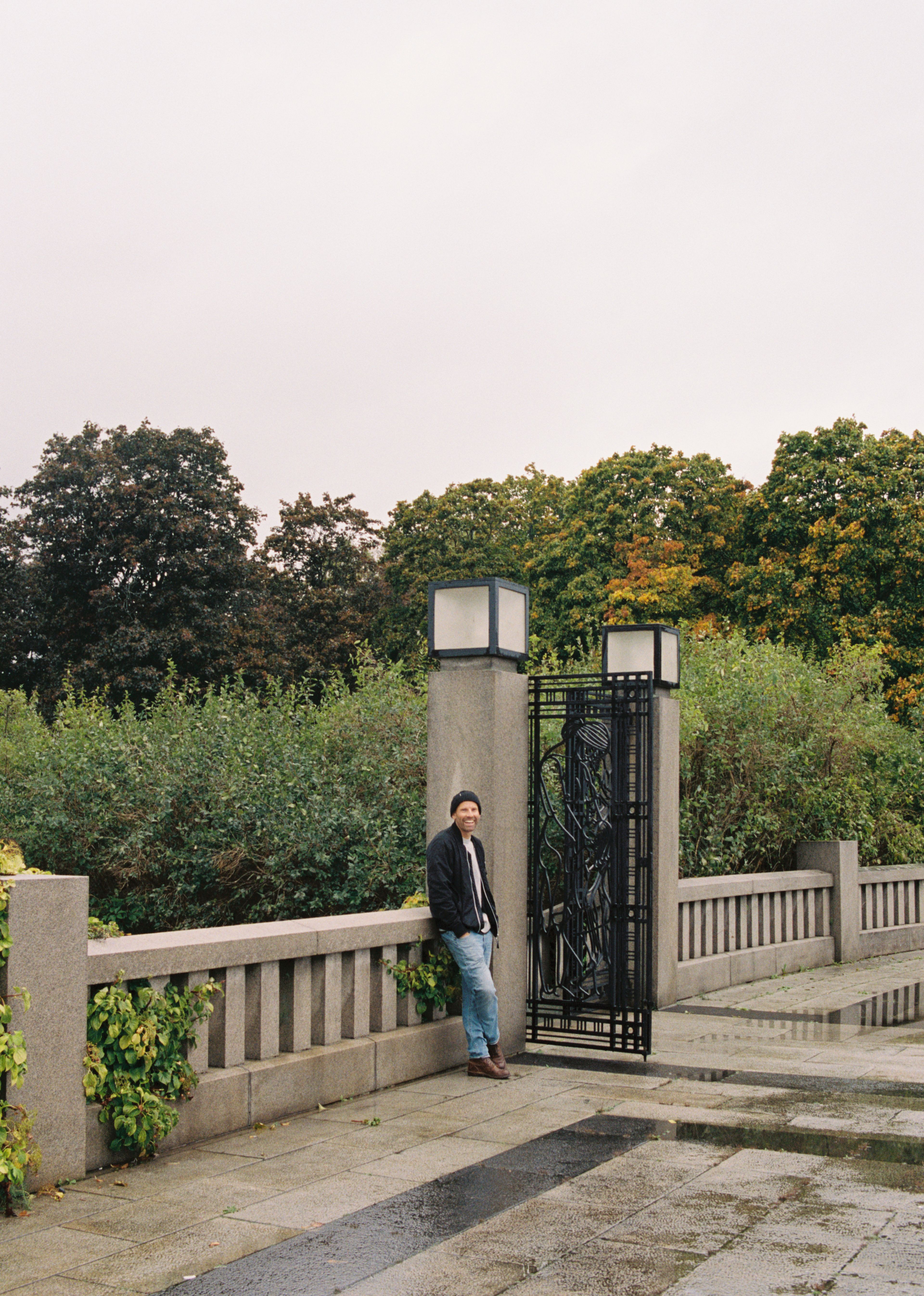 Jonas Kinge Bergland står i Frognerparken. Han har på svart jakke, svart lue og olabukse, og lener seg mot et rekkverk i stein.