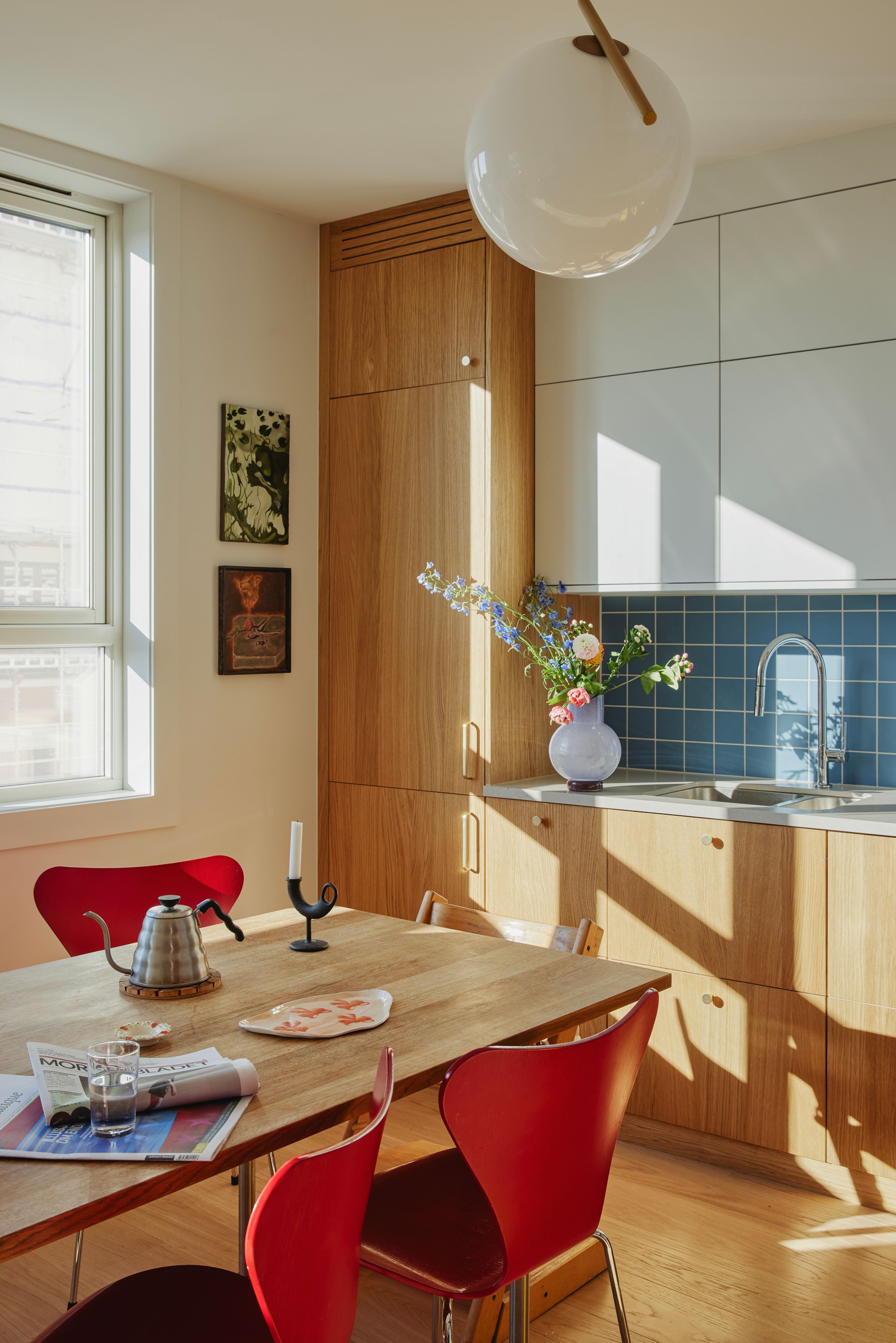 Kjøkkenfrontene er kledd i eik og på veggen er det montert blå fliser. Det er røde syverstoler rundt spisebordet i eik.