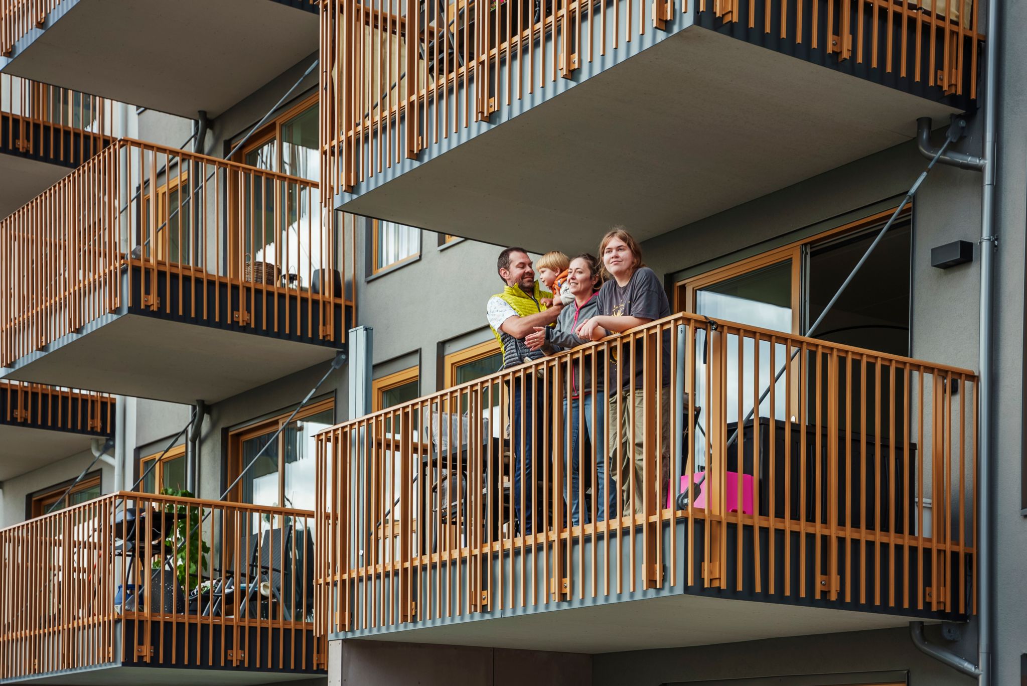 Maja og Nikola med sønn og datter står på en balkong mot en gråfarget blokk og ser utover.