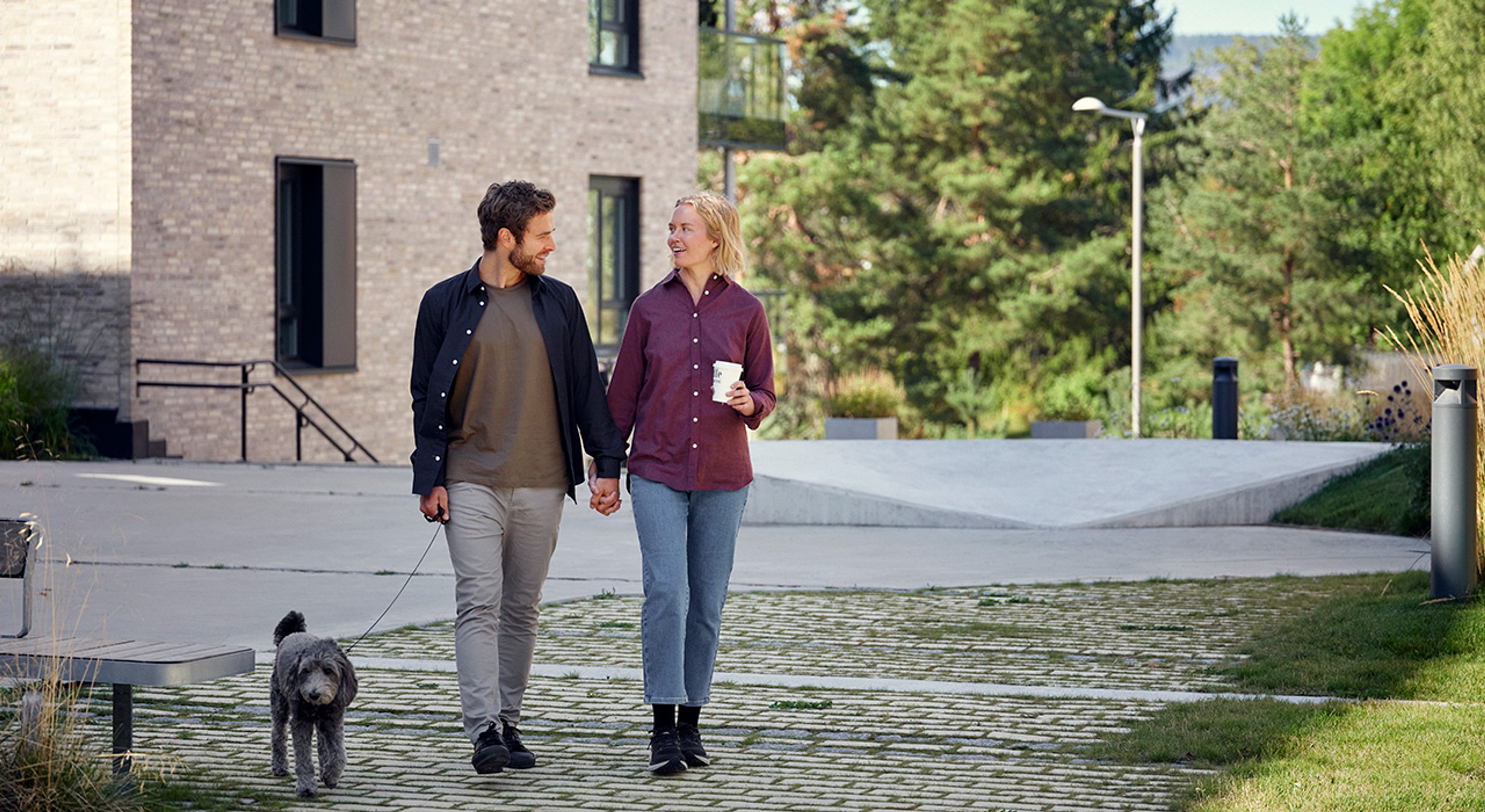 Foto av et par som går tur med hunden med kaffe i hånden.