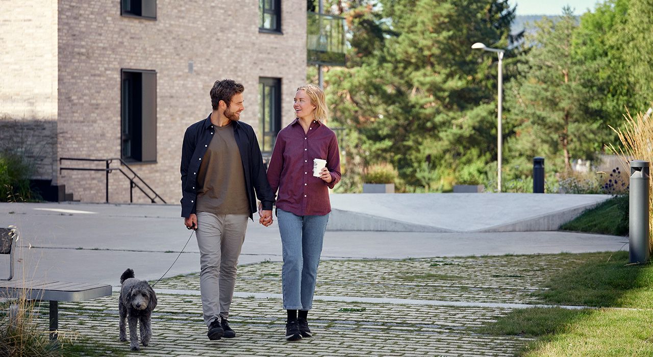 Foto av et par som går tur med hunden med kaffe i hånden.