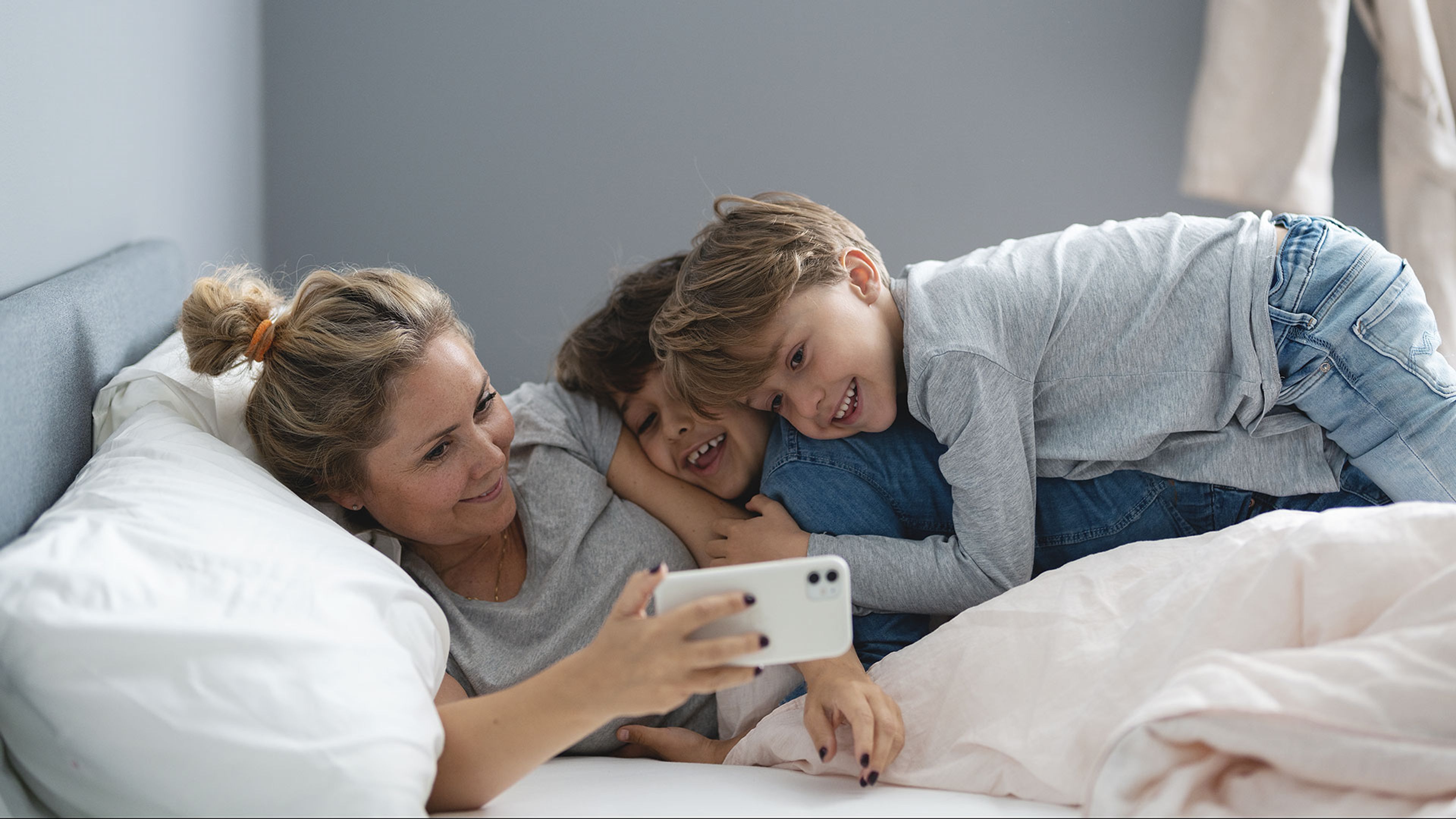 mamma och två barn tittar på telefon i sängen