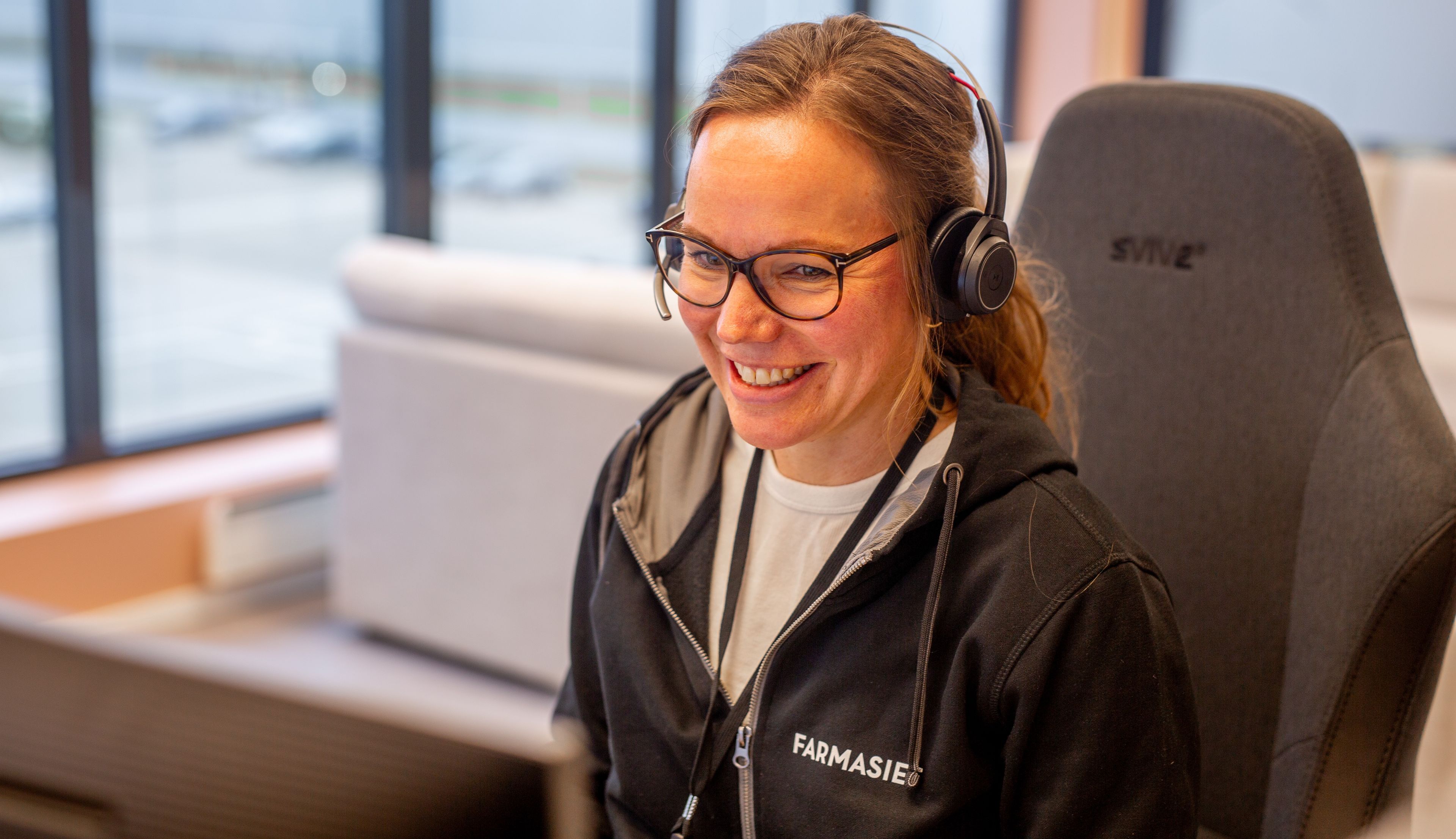 En dame fra kundeservice hos Farmasiet snakker i telefonen og smiler.