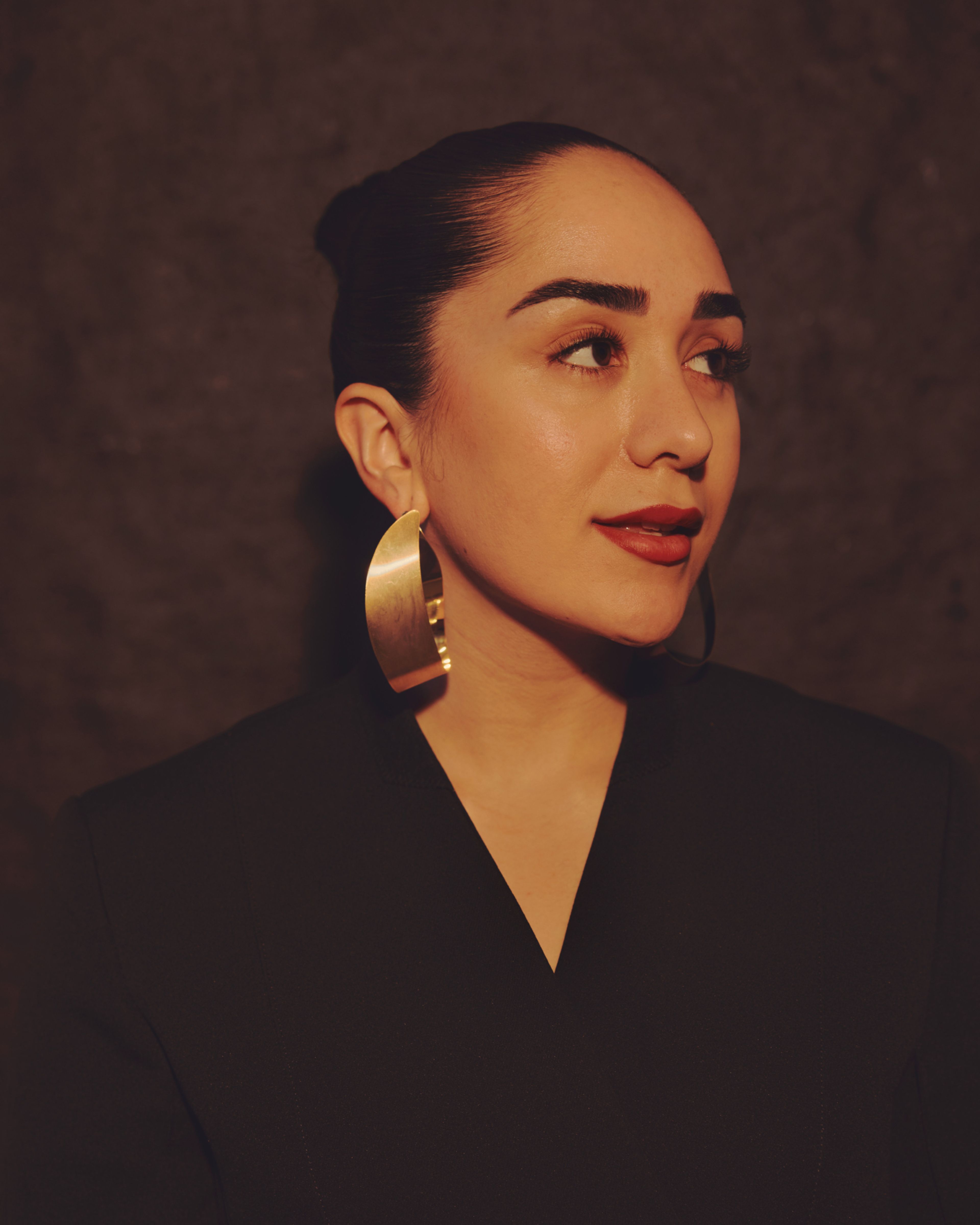 Portrettbilde av Amanda Delara. Hun har håret i en stram knyte og har store gulløredobber i ørene. Hun er pent sminket og ser mot venstre.