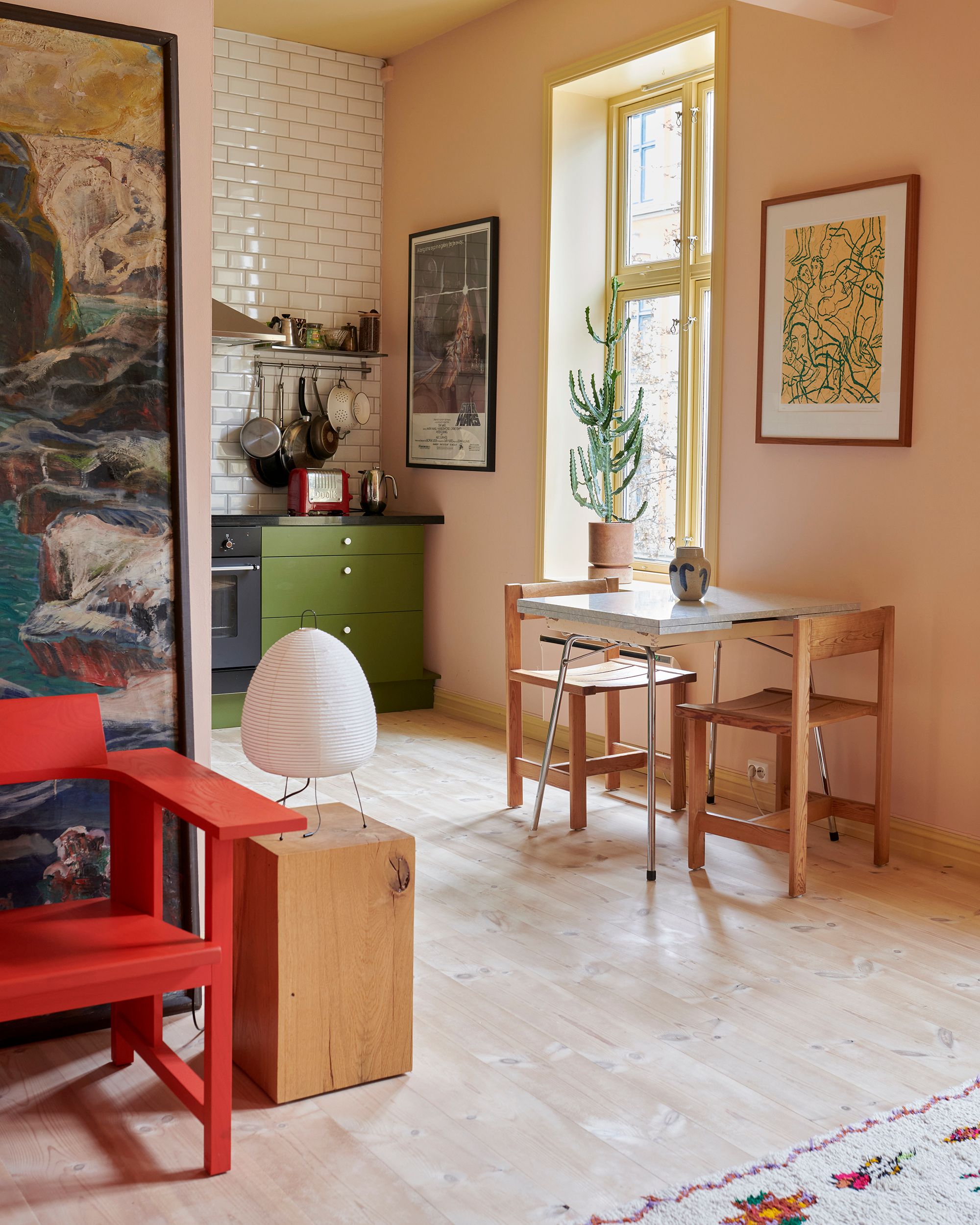 Grønt kjøkken med spisebord inntil en rosa vegg. Rød stol og et bilde i forgrunnen til venstre.