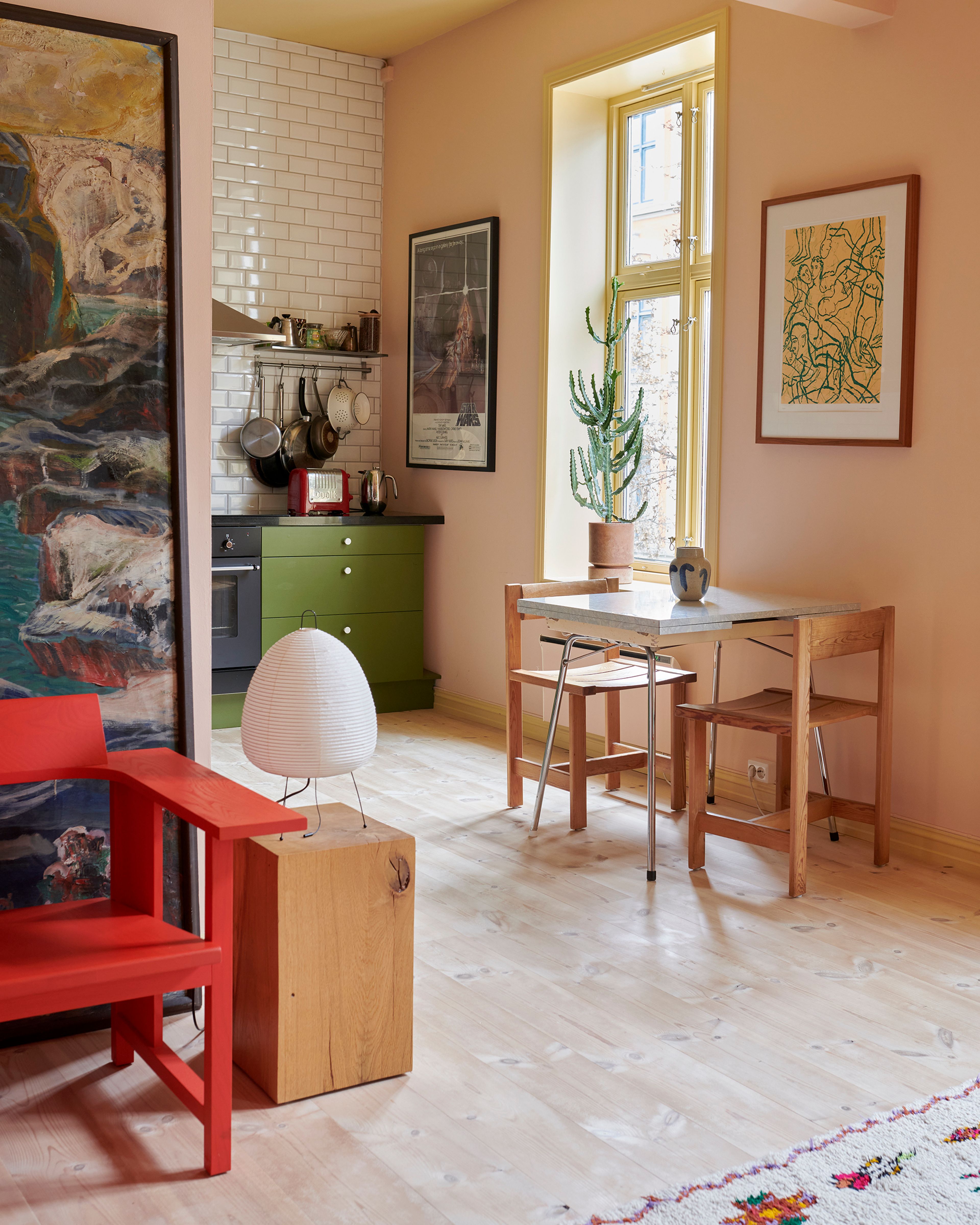 Grønt kjøkken med spisebord inntil en rosa vegg. Rød stol og et bilde i forgrunnen til venstre.