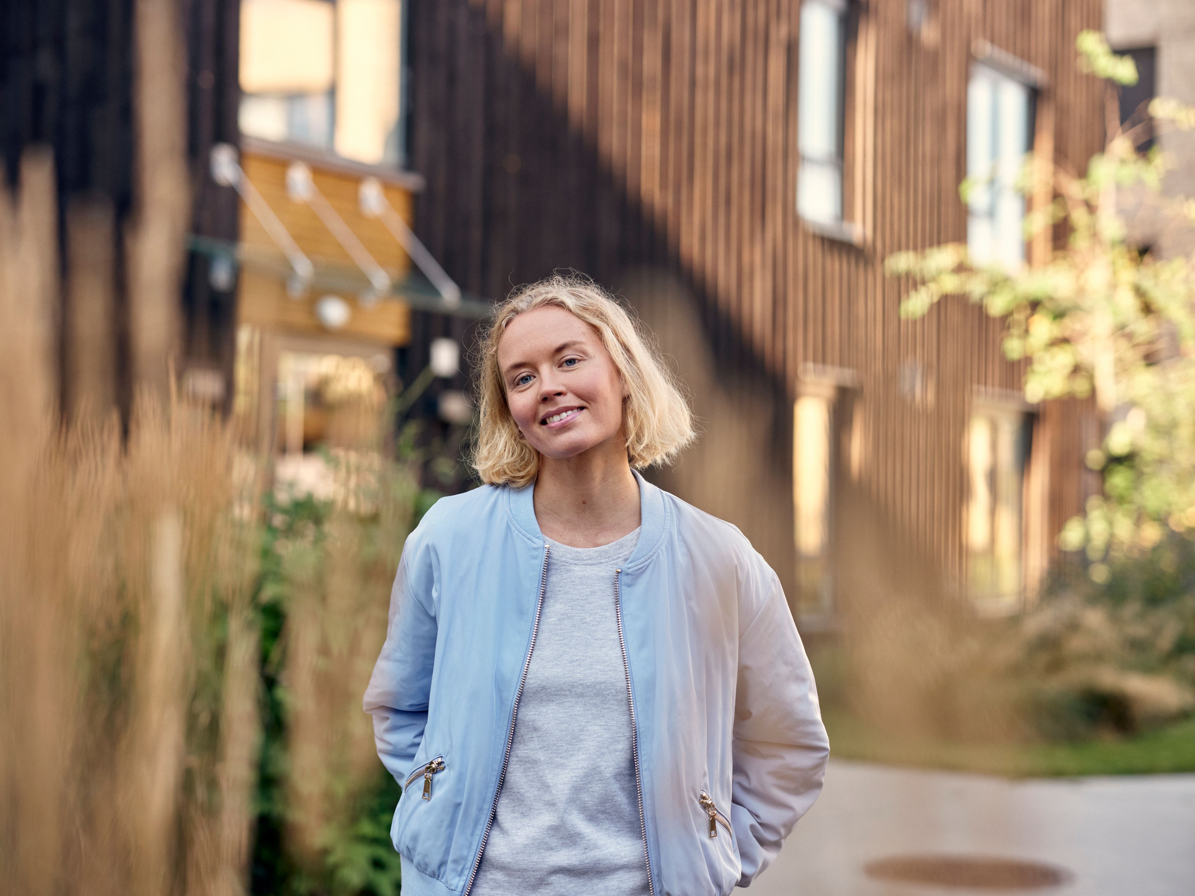 Ei ung dame står ute i nabolaget sitt og smiler til kameraet.