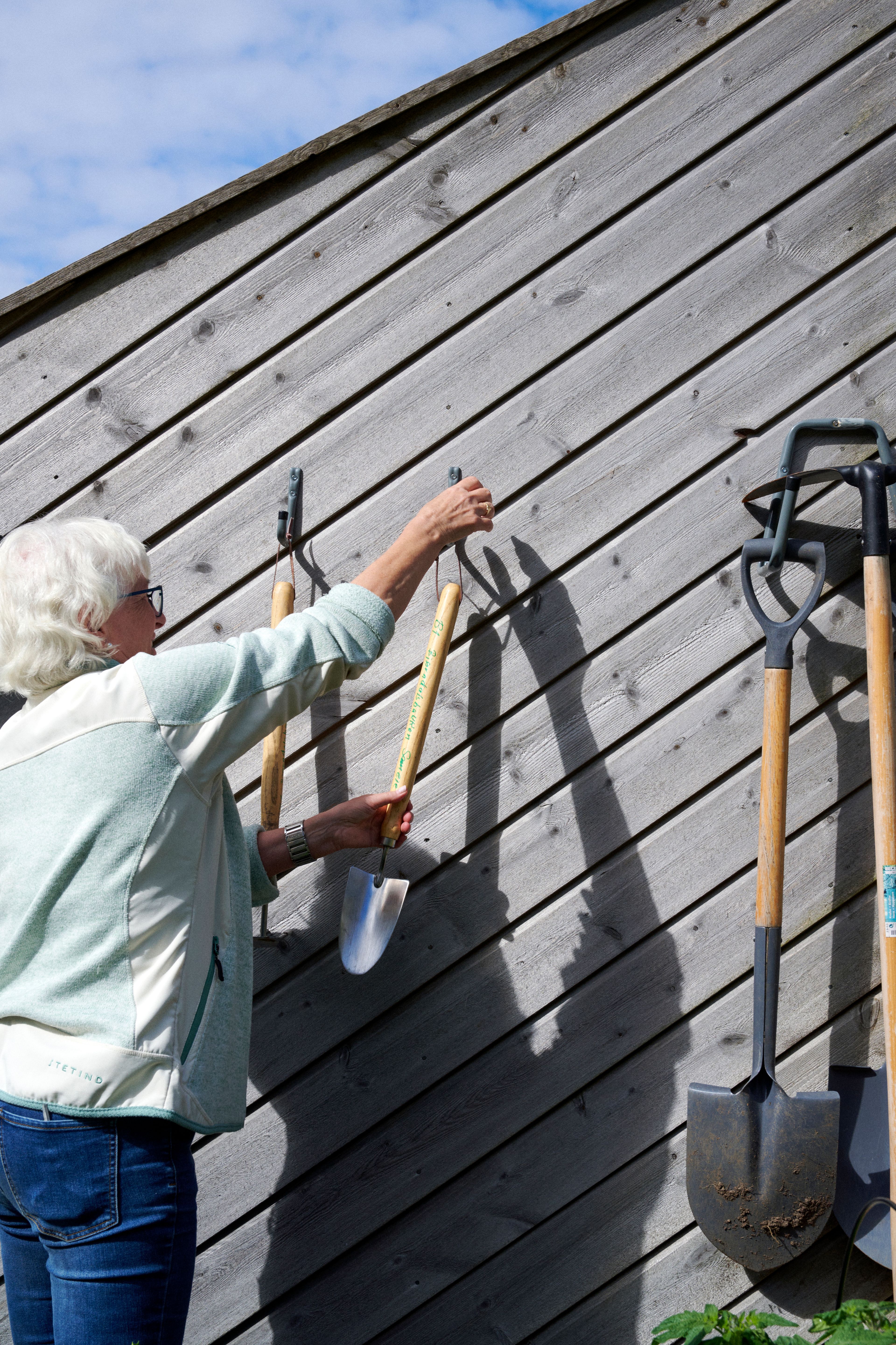 Kvinne henger opp hageredskap på knagger på en utendørs vegg.