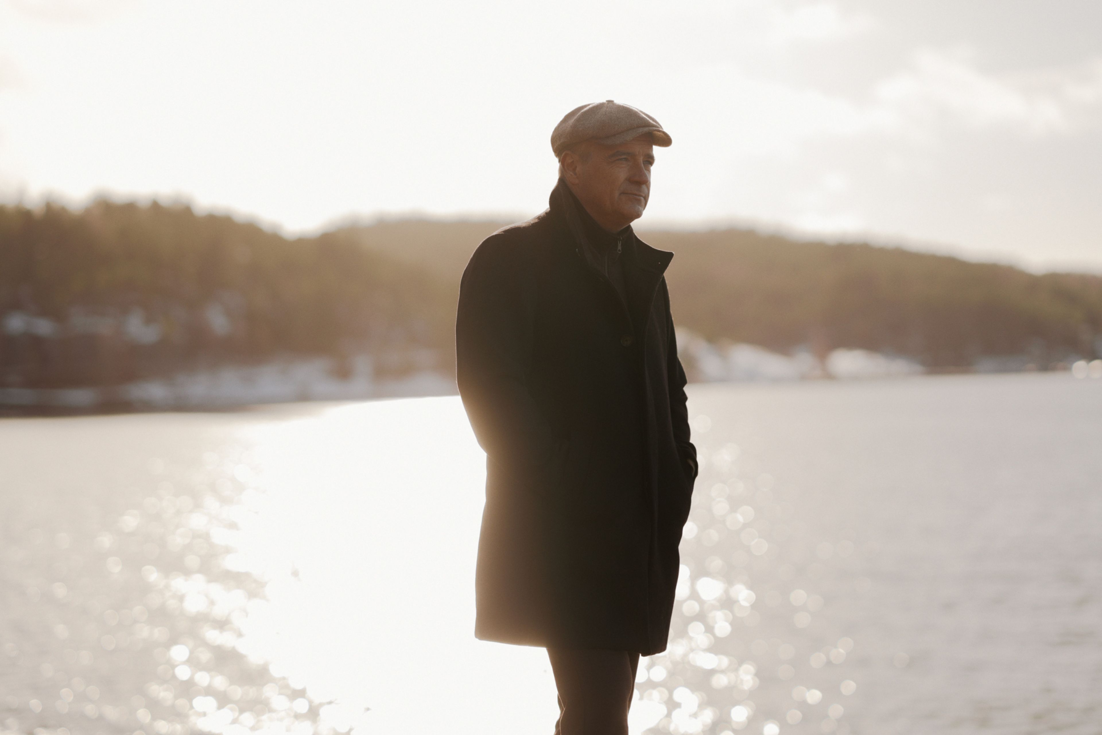 Bilde av Odd René Andersen med six pence og frakk. Han står foran et stort vann.