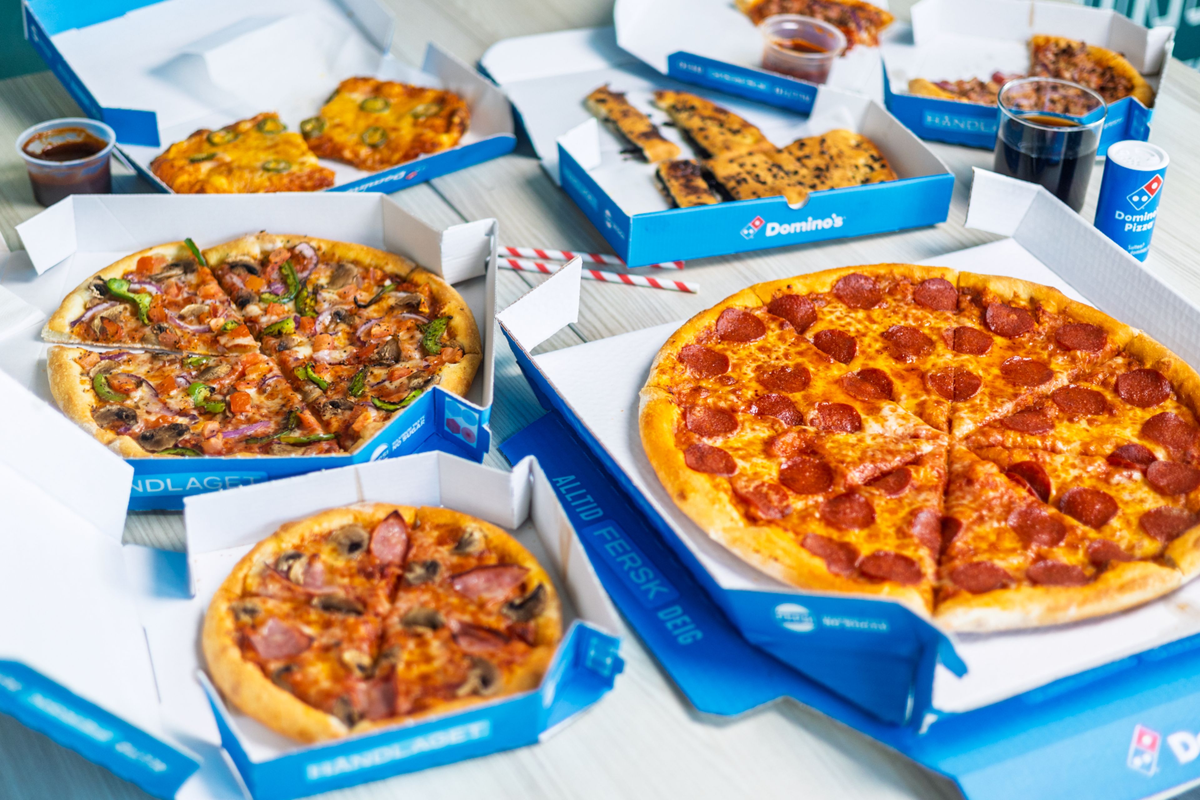 På bildet ser du flere pizzaer rundt et bord. Det er forskjellig tilbehør, som eksempelvis Pepperoni.