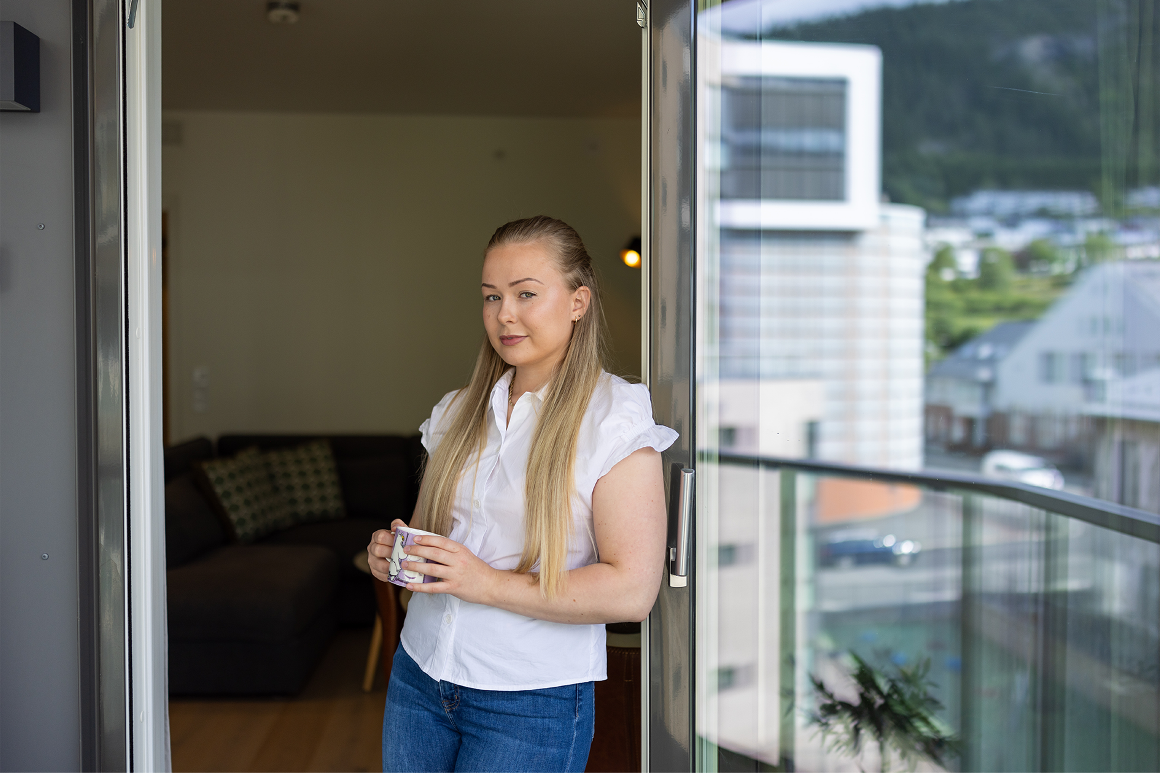 Amanda står lent inntil dørkarmen på terrassen sin, med stuen i bakgrunnen.