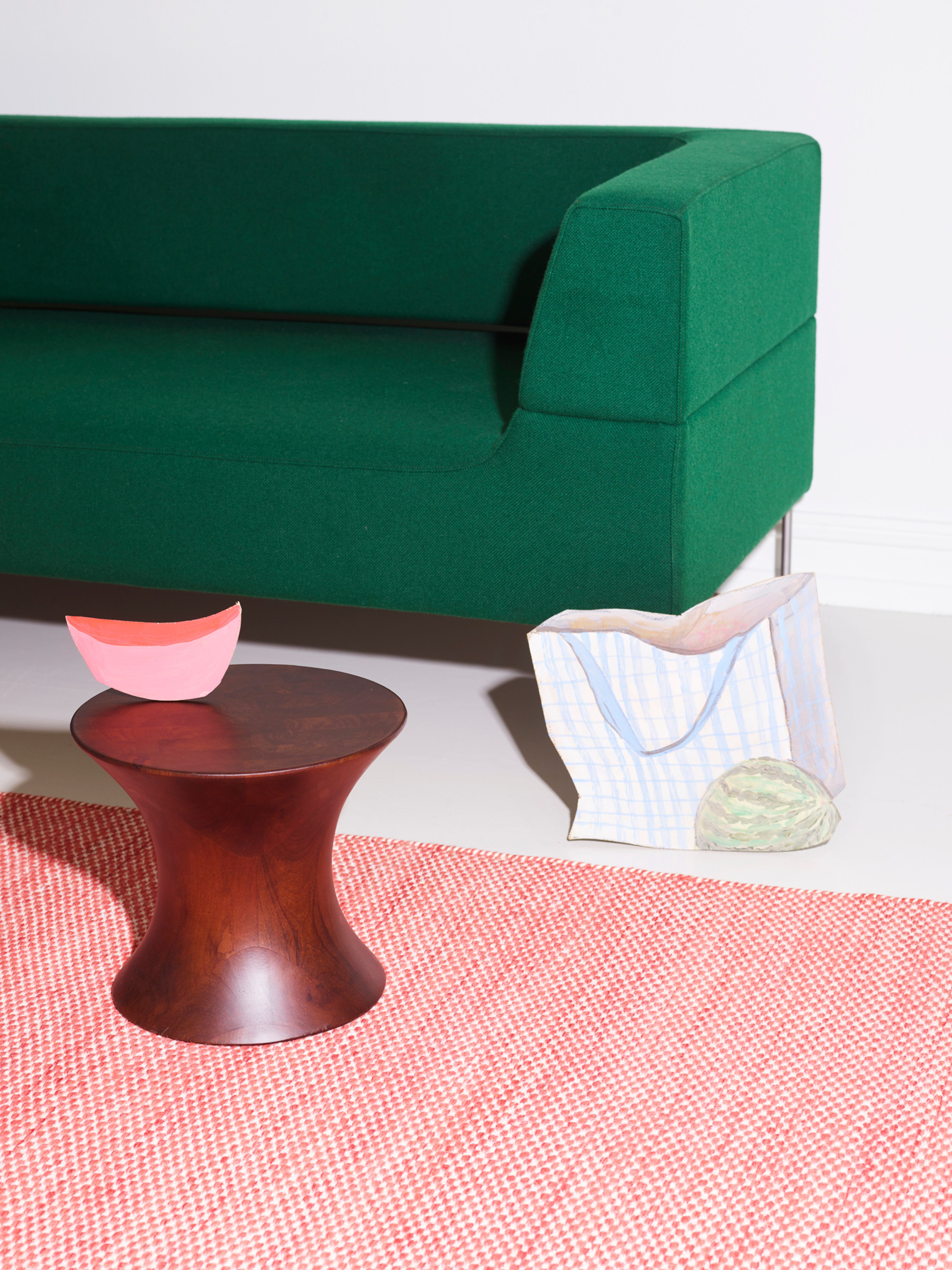 Grønn sofa, rosa teppe og et lite sidebord i mørkt tre.