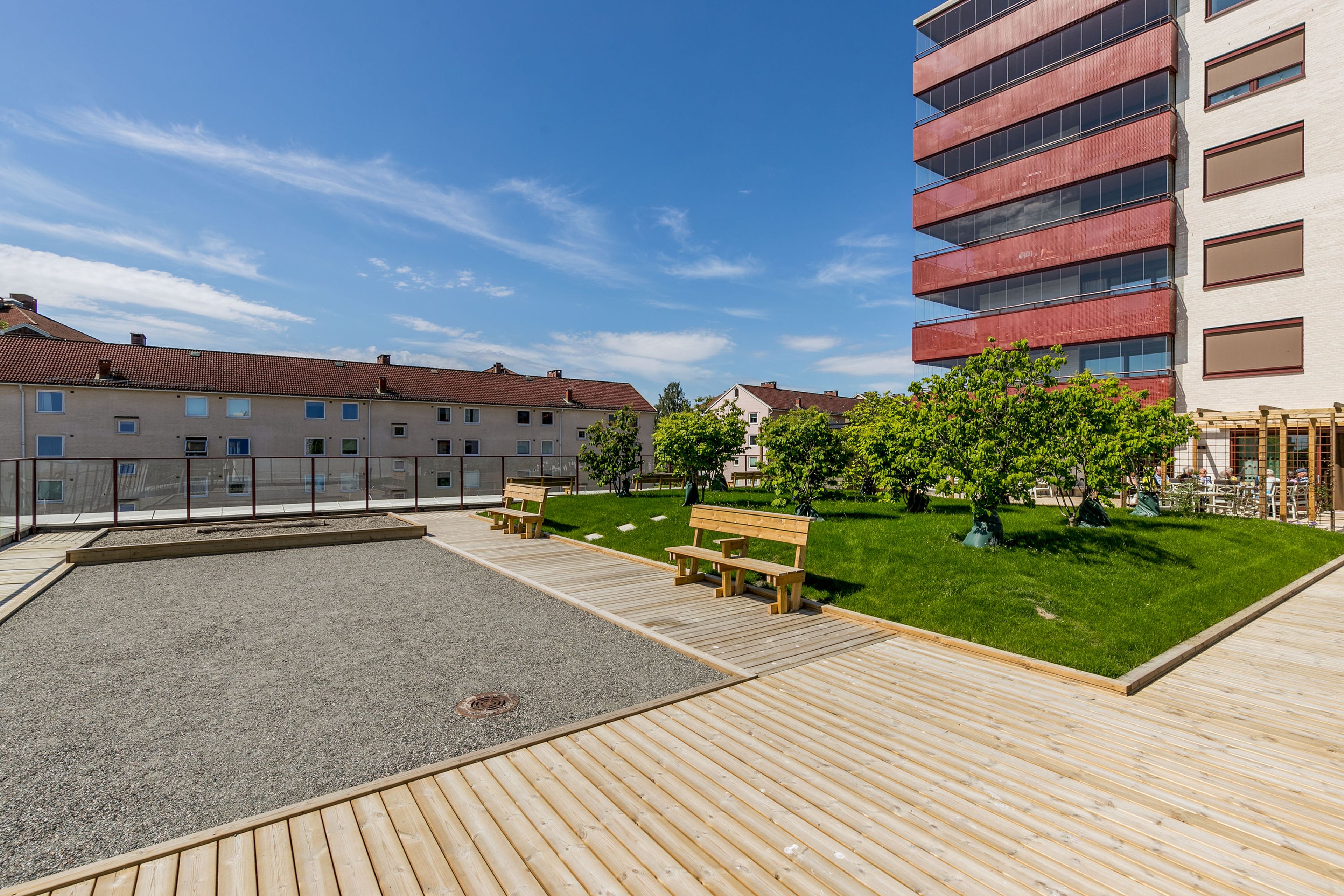 Felles takterrasse. Det er en gressplen, trær, boul-bane, benker og pergola.