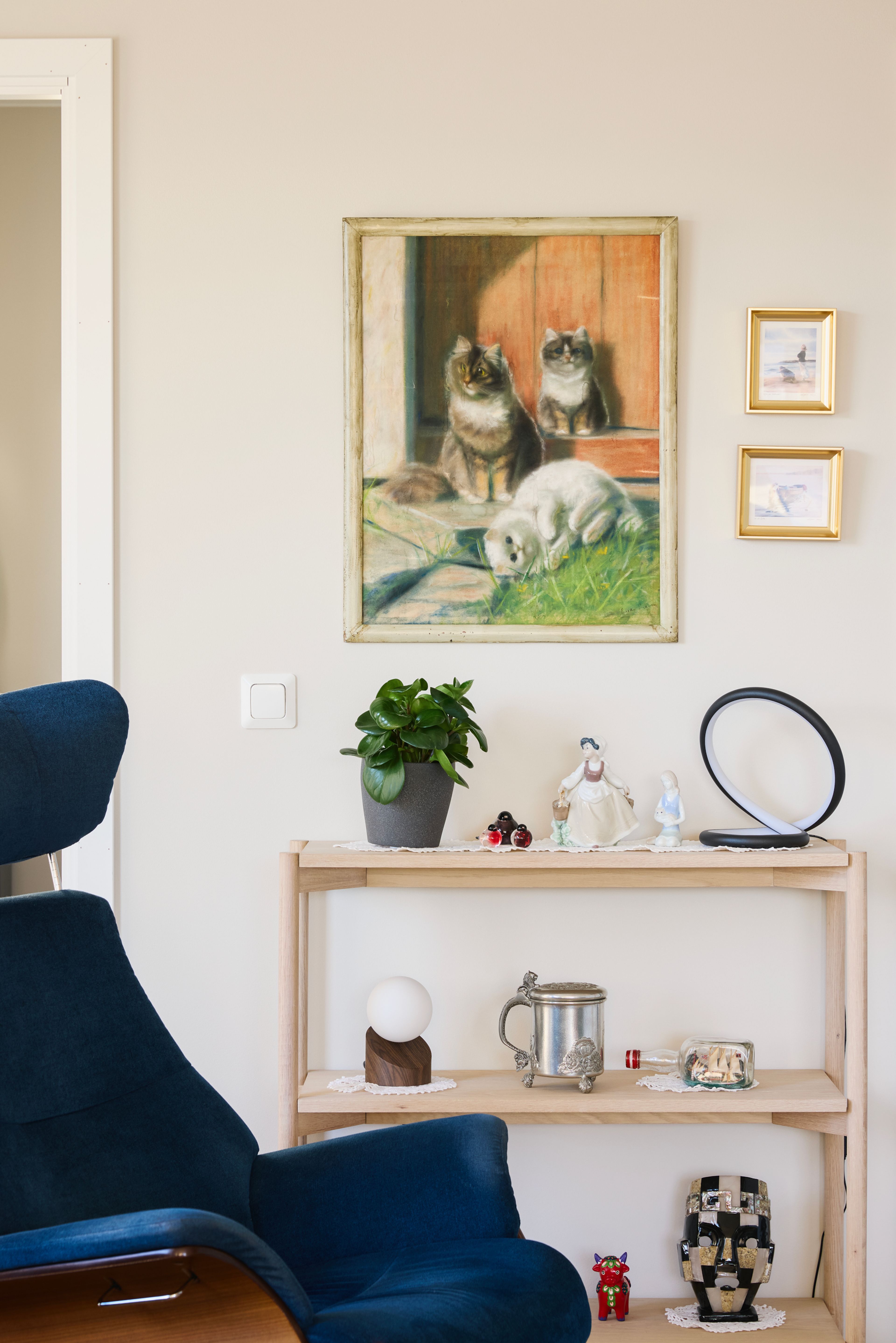Detaljbilde av en vegg med bilder og en hylle fylt med pyntegjenstander, foran står en blå stol