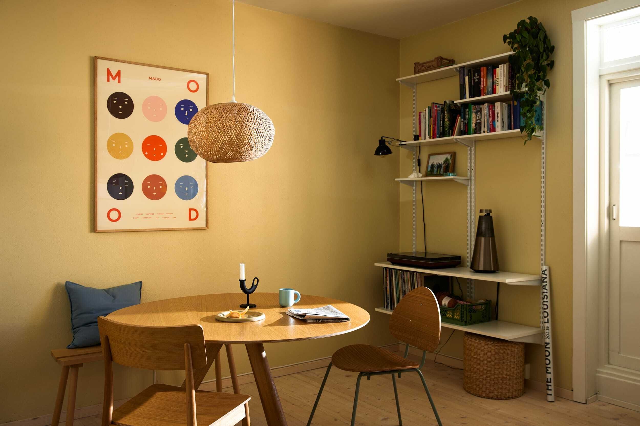 En del av stua med vegger malt i gul, spisebord og hyller.