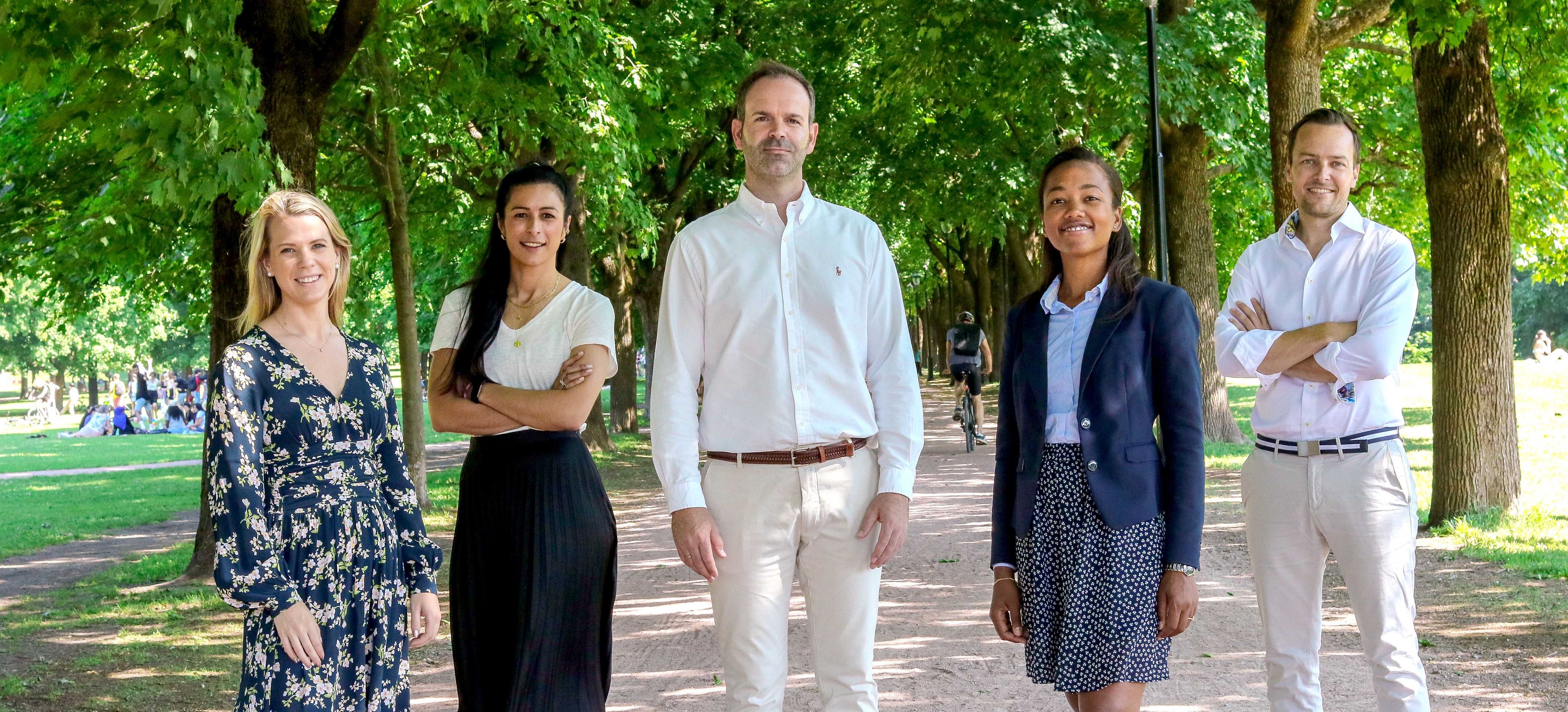 Fem mennesker står i en grønn park og smiler til kamera.