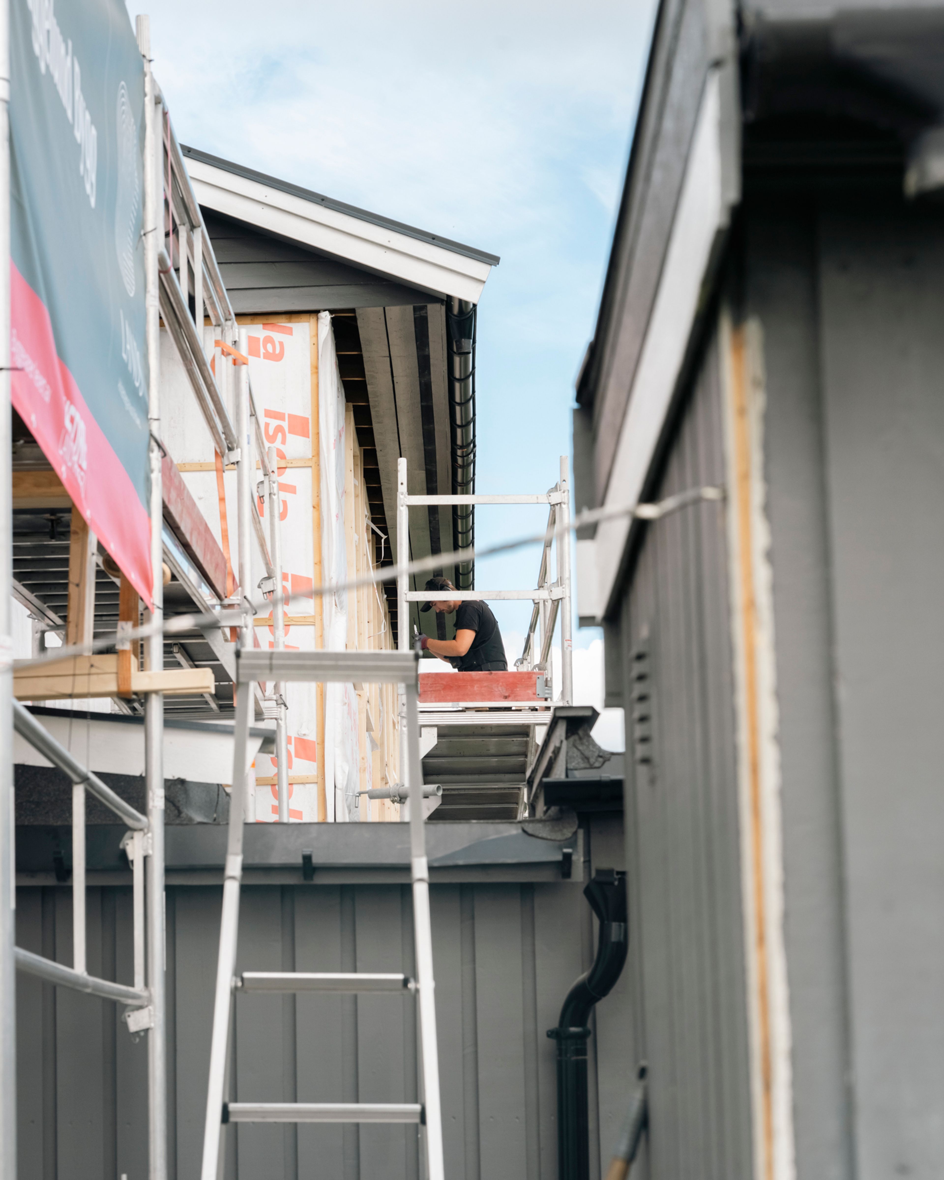 En snekker jobber på stillas under rehabilitering av rekkehusfasaden i Delfinen borettslag.