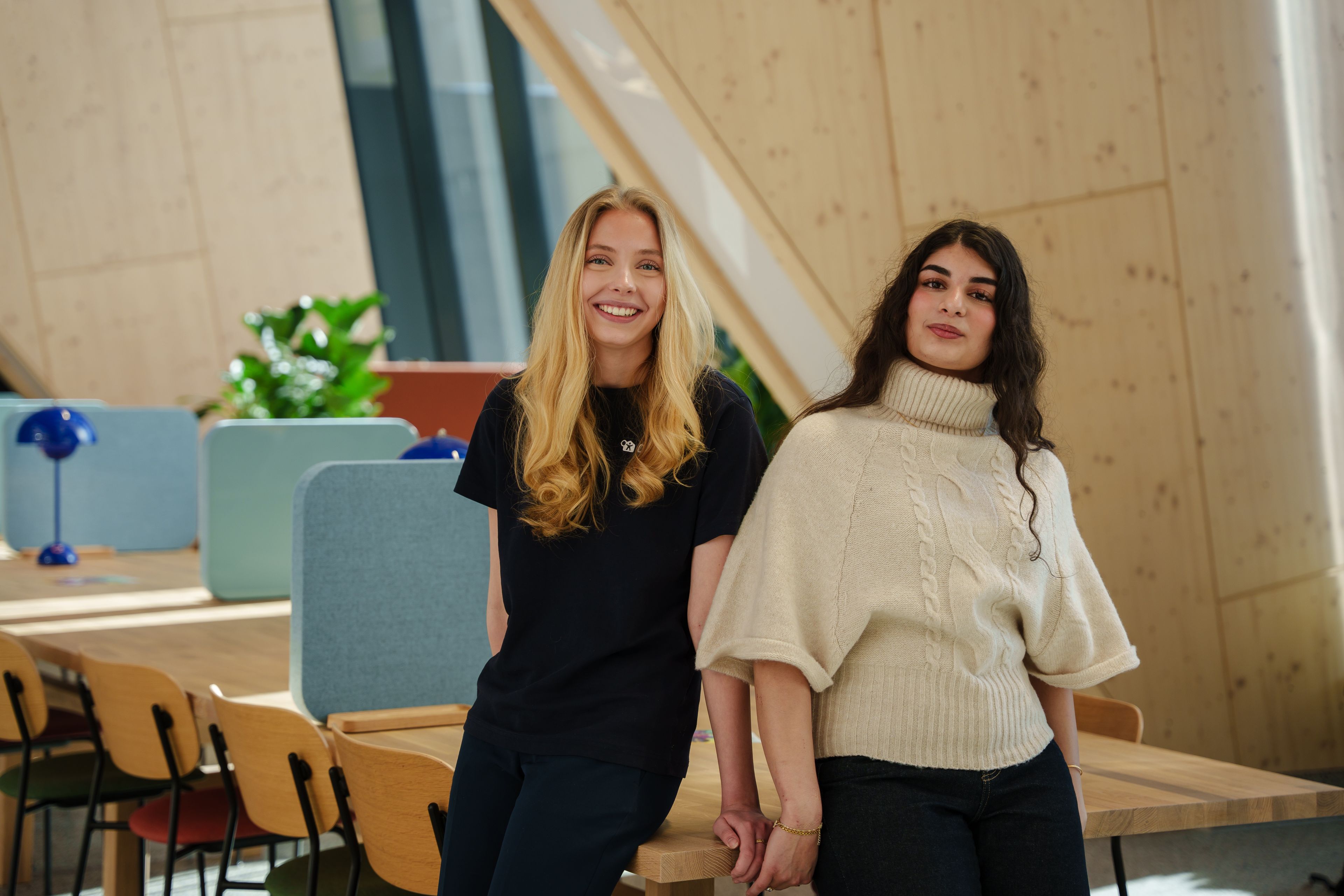 To tenåringer står og smiler mot kamera i et stort kontorlokale