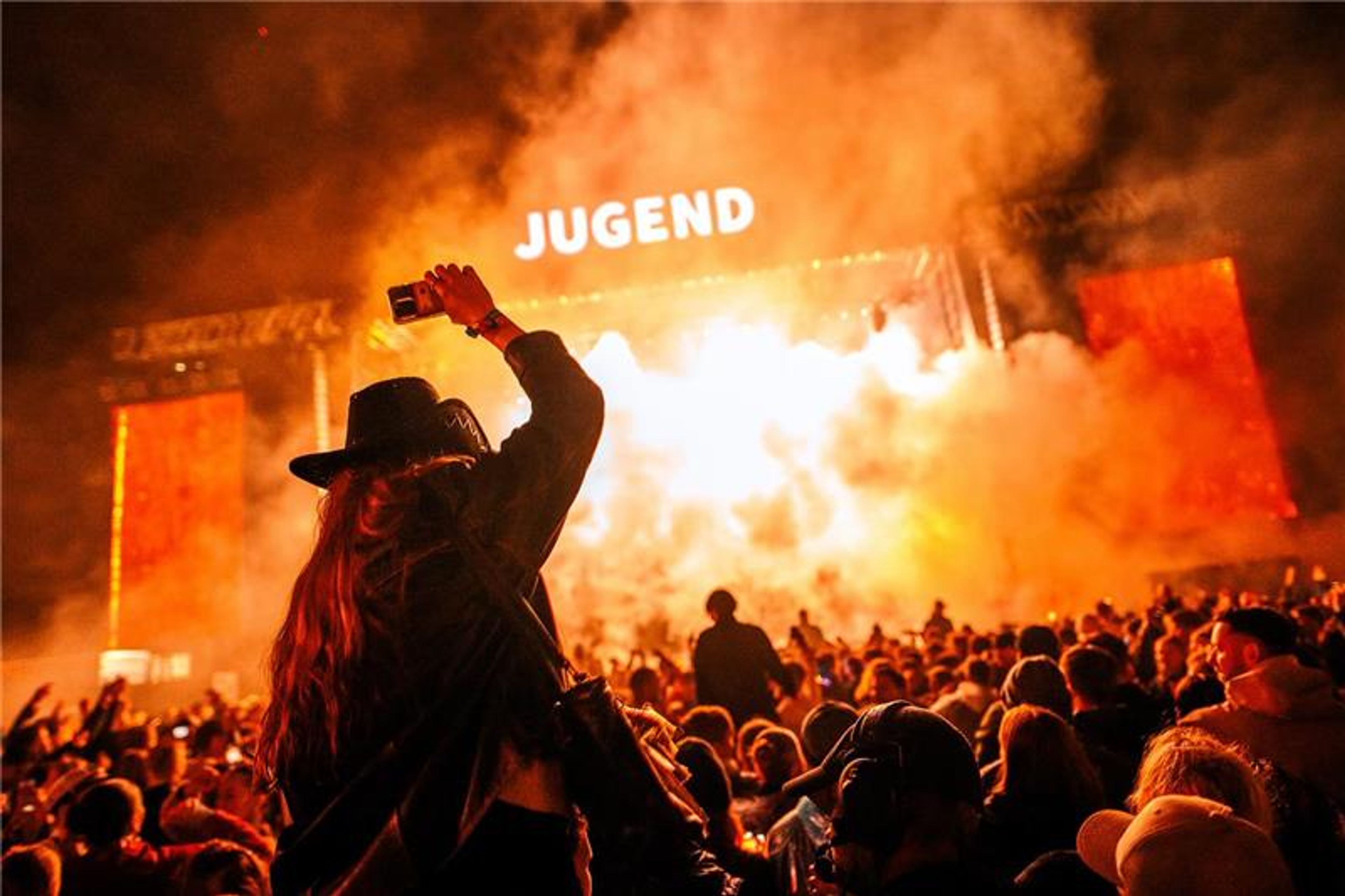 Festivalscenen på Jugend. Det er flammer fra scenen og en person sitter på skuldrene til en annen og holder hånden opp i været.