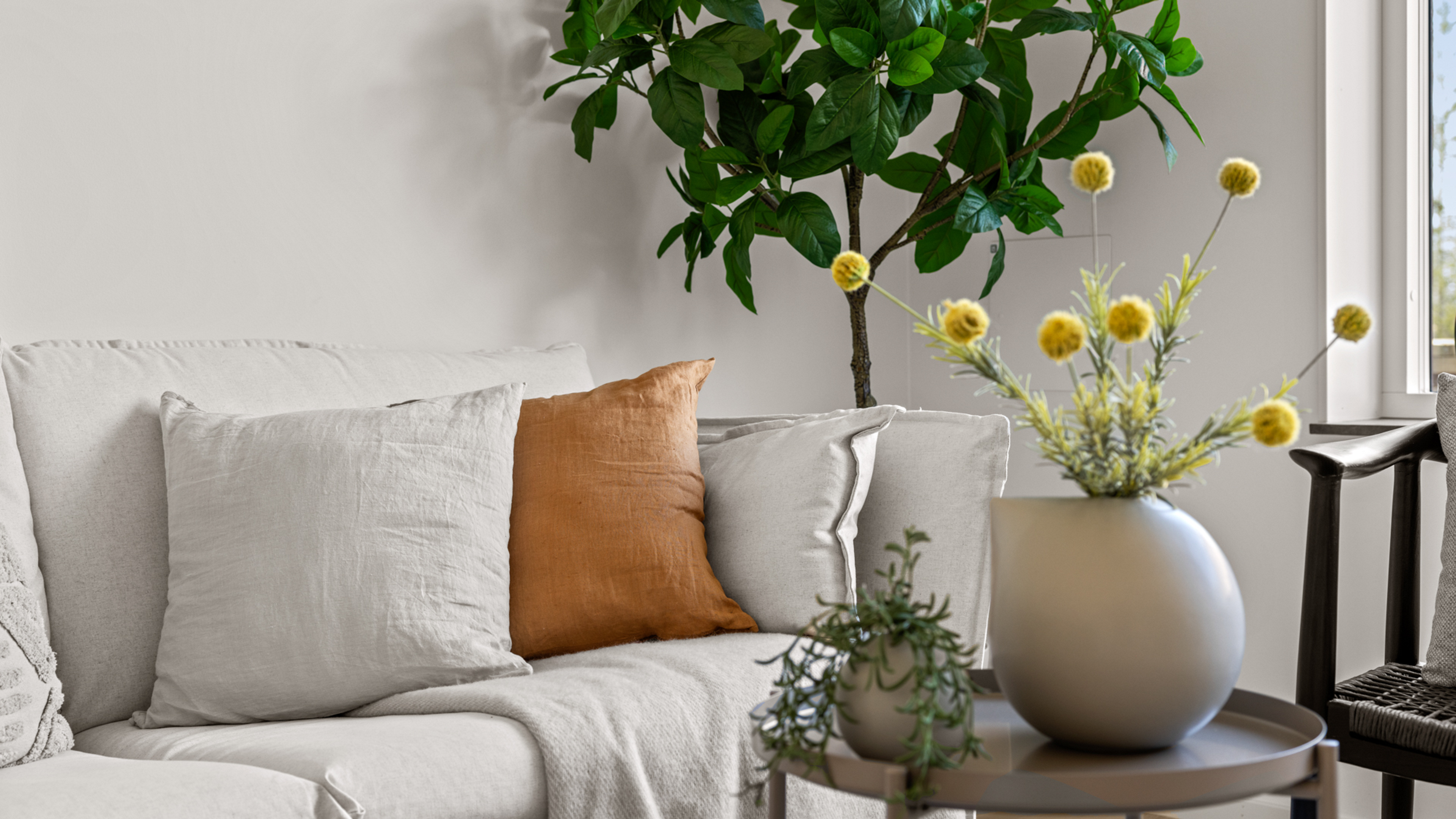 Inzoomad bild på ljus soffa med ljus och orange kuddar, med ljus blomkruka i förgrunden