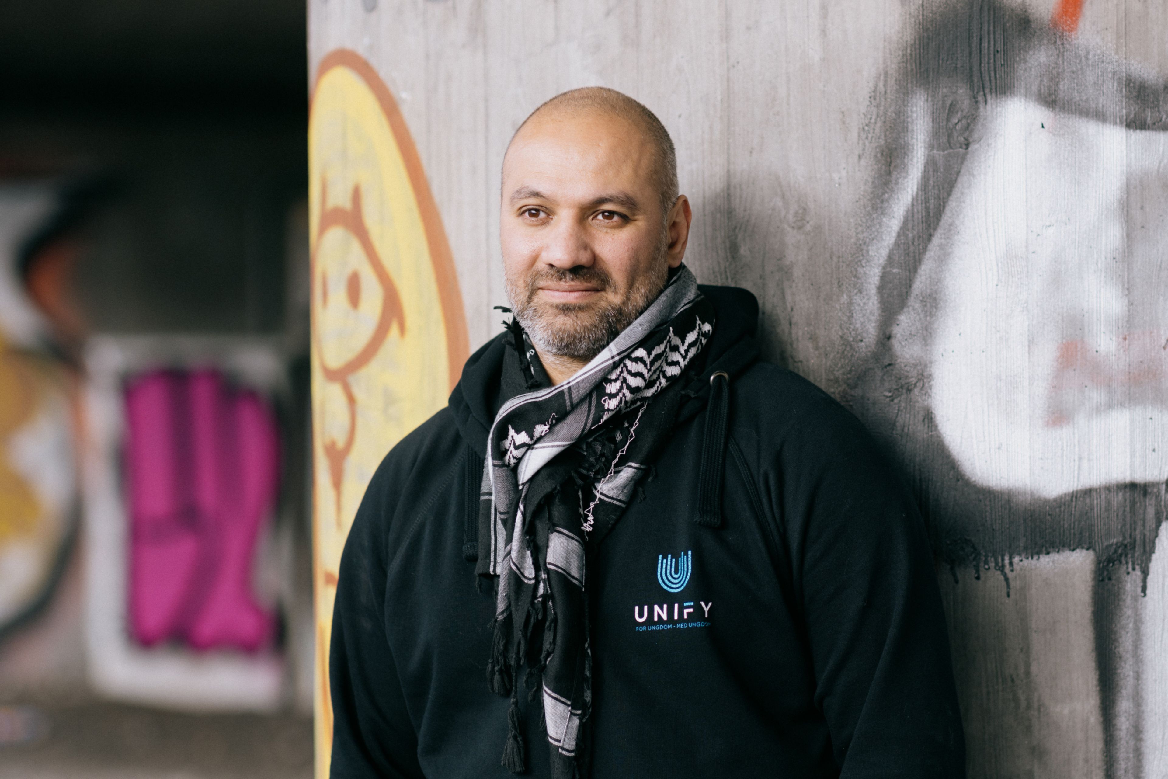 Bilde av Marco Elsafadi som står inntil en murvegg og har på seg hettegenser og palestinaskjerf