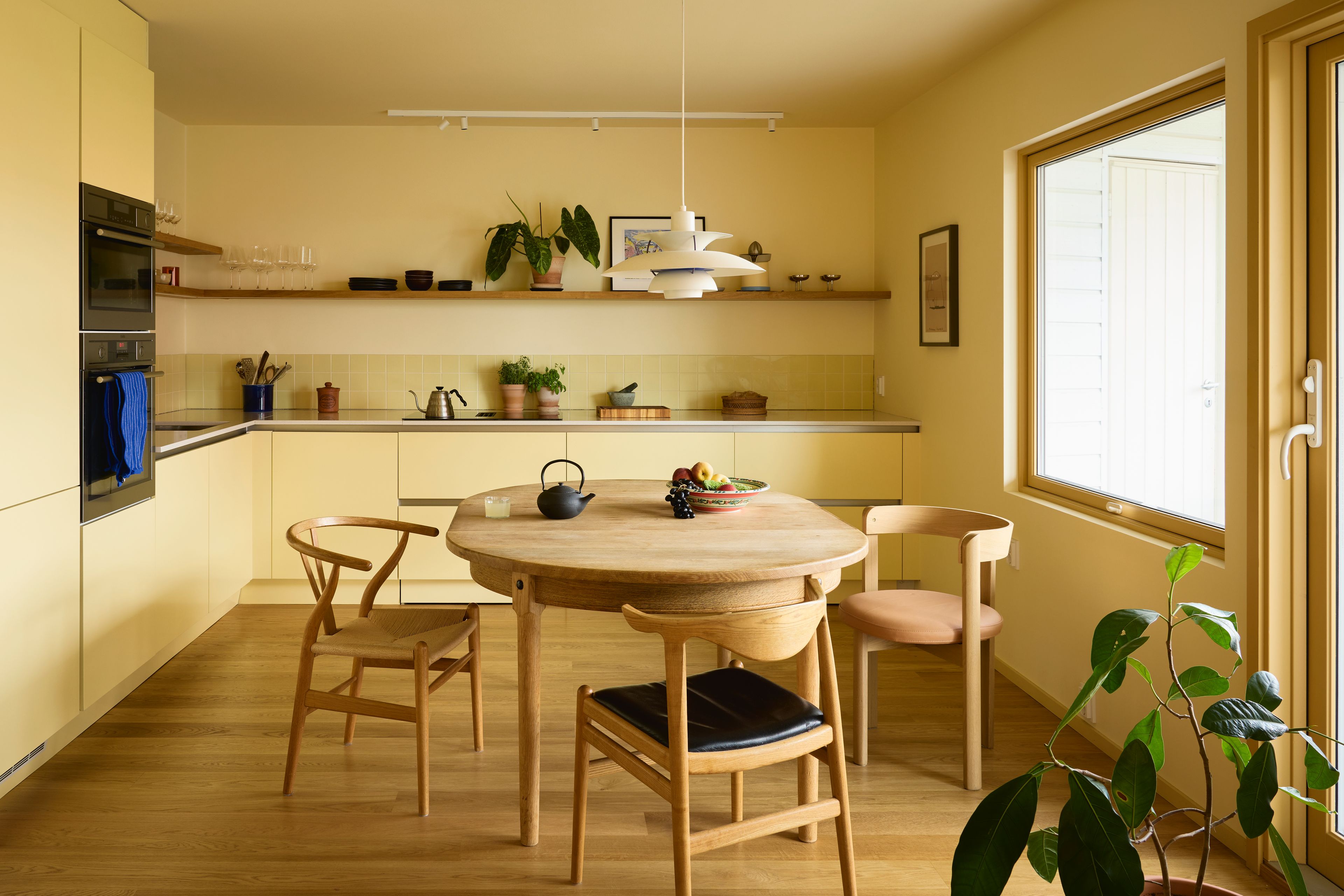 Oversiktsbilde av et gult kjøkken med spisebord med stoler i eik.