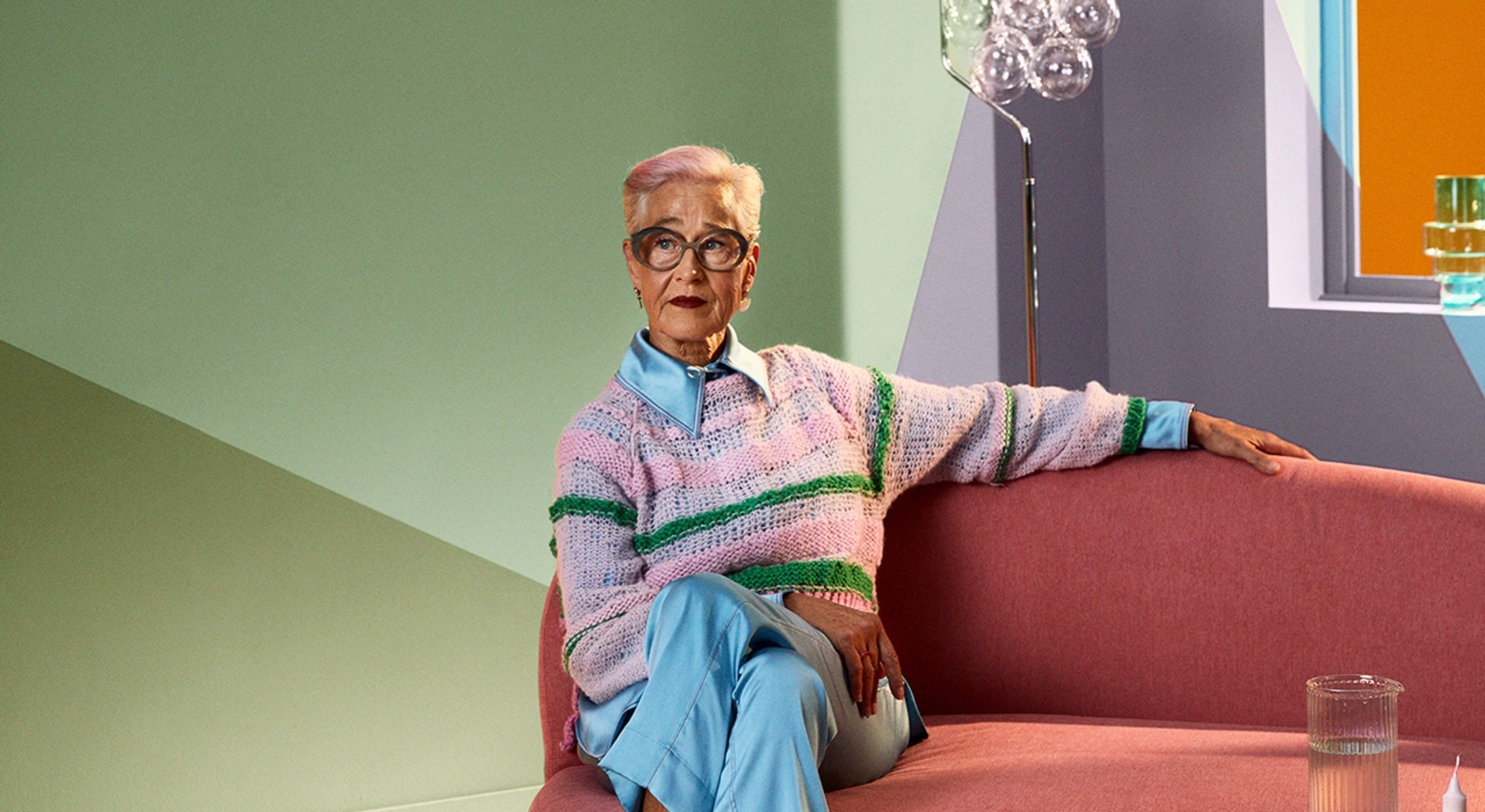 Eldre dame i sofa med mange spenstig farger på veggene.