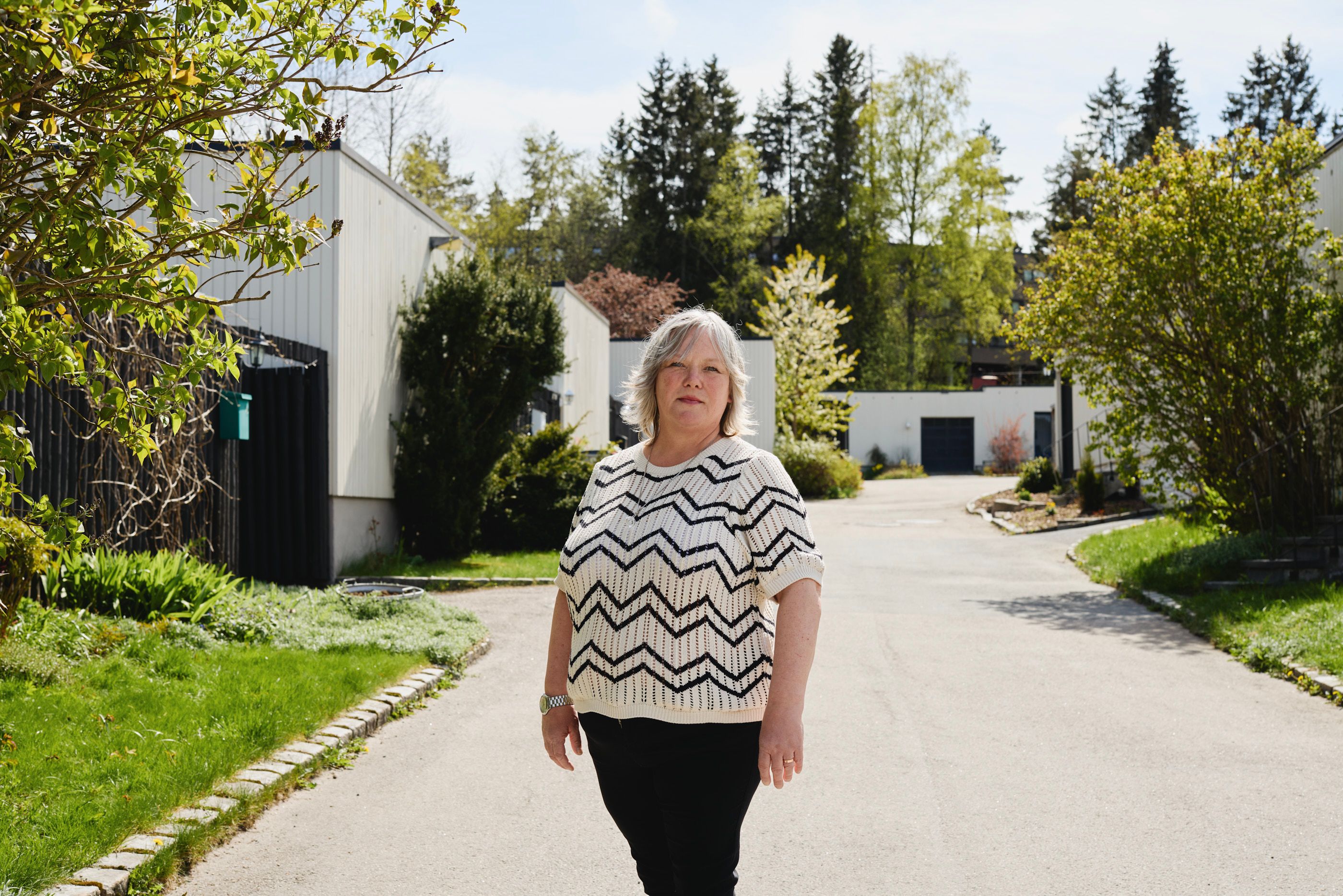 Chera Westman står i et grønt boligområde med rekkehus i bakgrunnen
