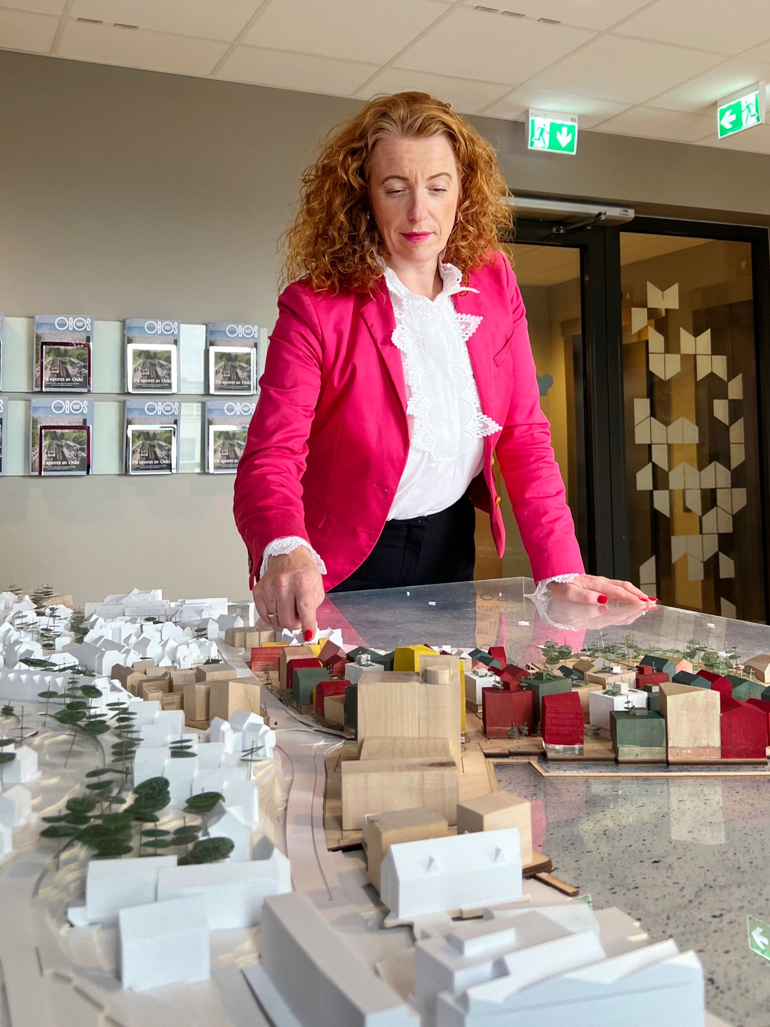 Kristin står og lener seg over en modell av Kronstadparken inne på et kontor, og peker på et par av byggene.