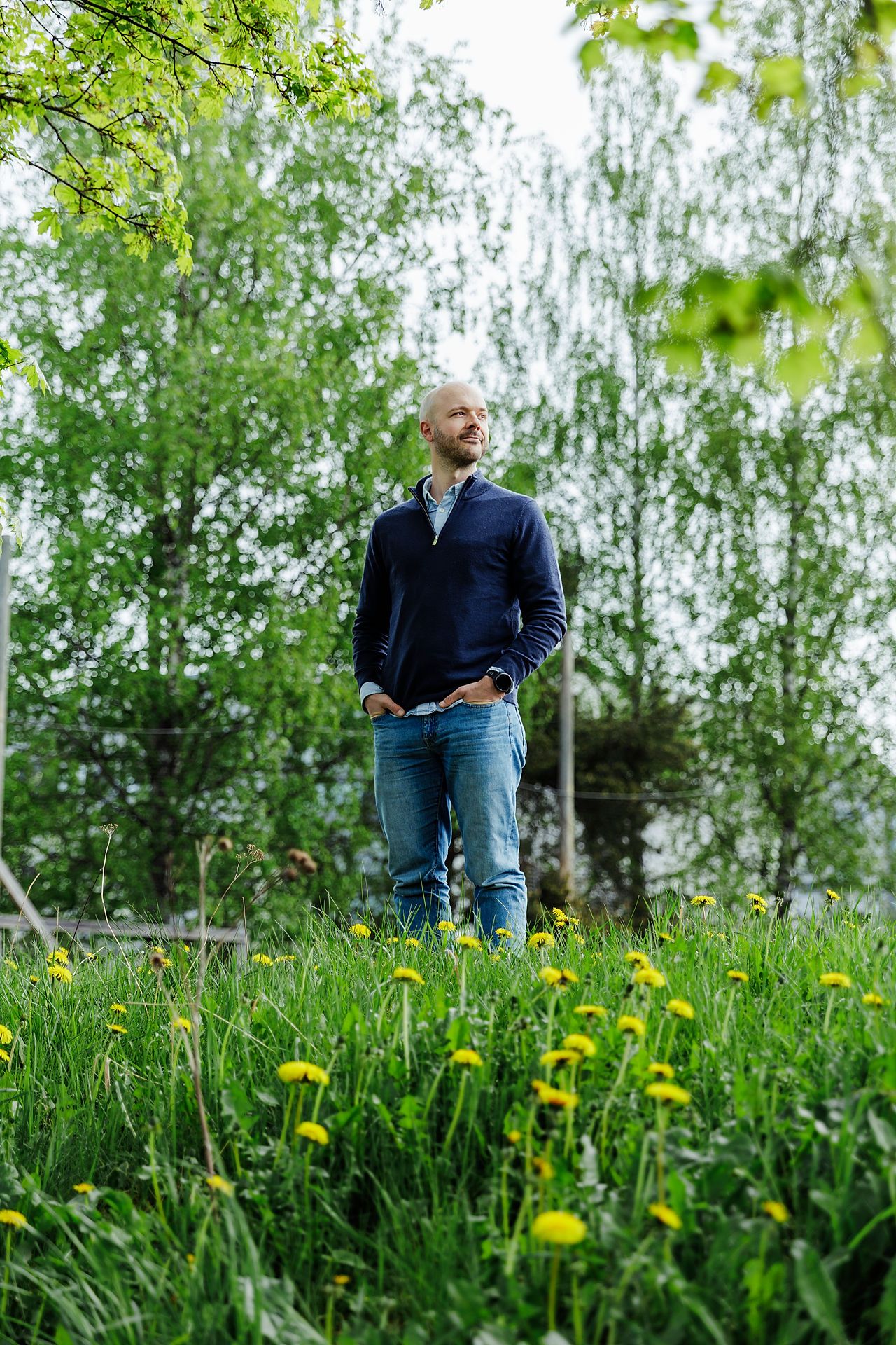 Simen står i en gressbakke med løvetann og furutrær rundt.