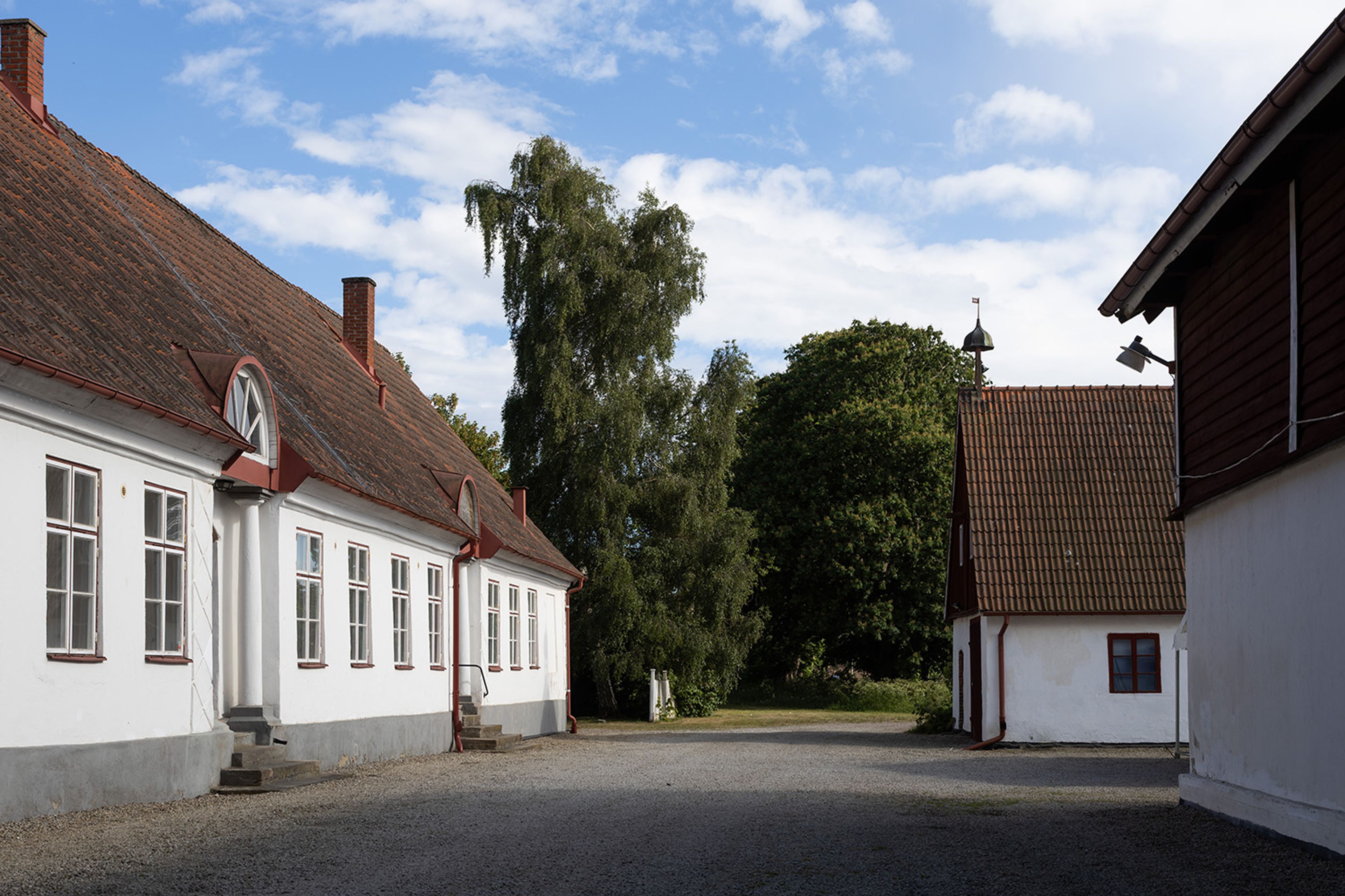 Foto på gårdsbyggnader med vit puts och röda tegeltak