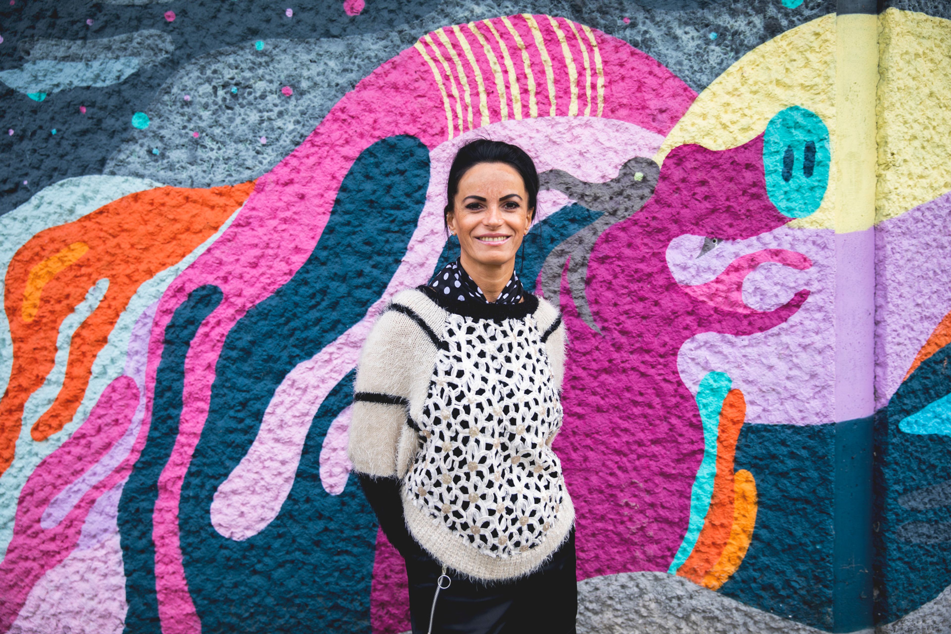 Mihaela står foran en fargerik vegg og smiler mot kameraet.