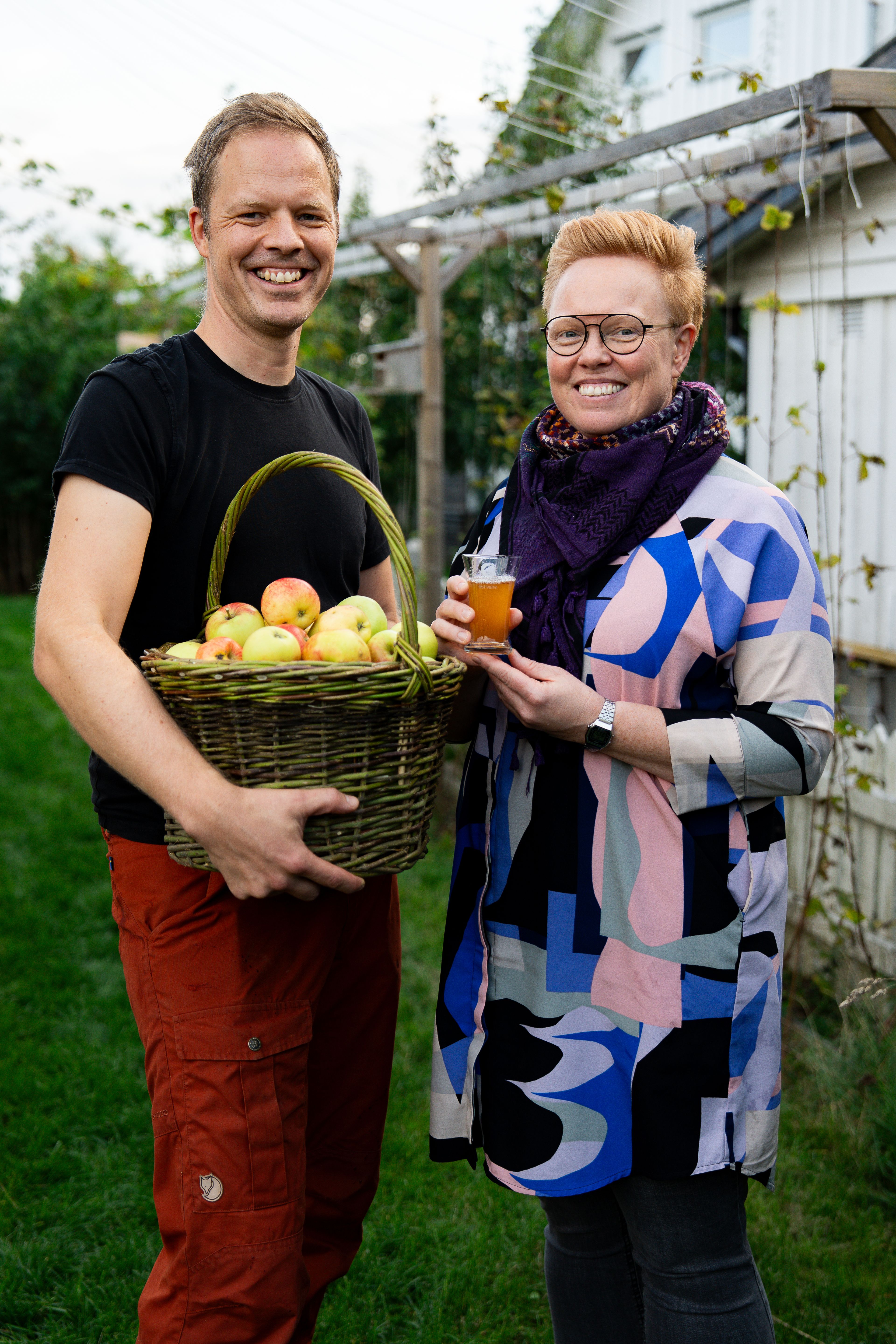 Menn og kvinne står med en eplekurv i en hage og smiler mot kamera