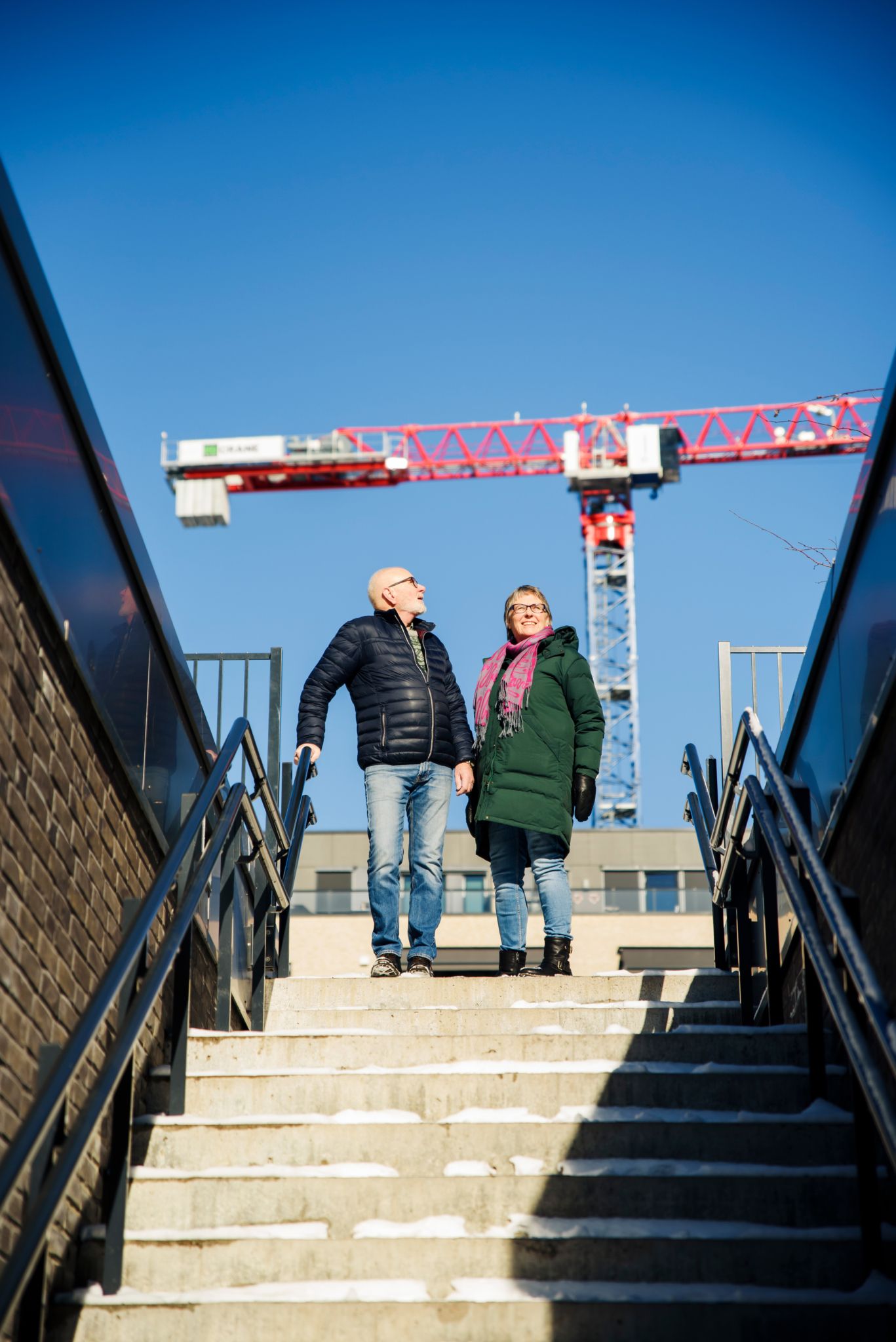 Frank og Ellinor Sengebusch står i en trapp med en rød kran i bakgrunnen