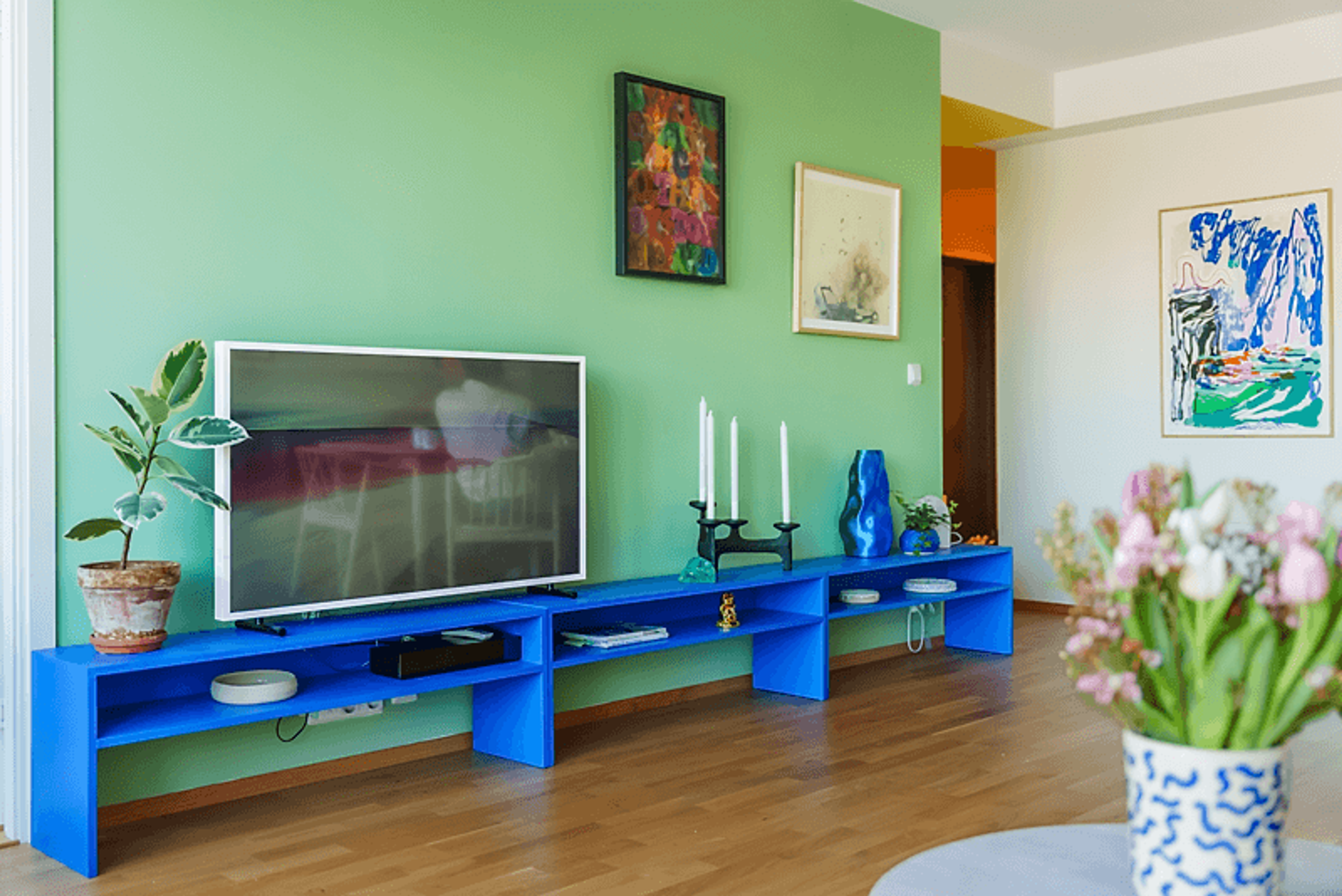 Oversiktsbilde av stueveggen til Ane som viser TV-en og de fargerike møblene, samt den grønne veggen