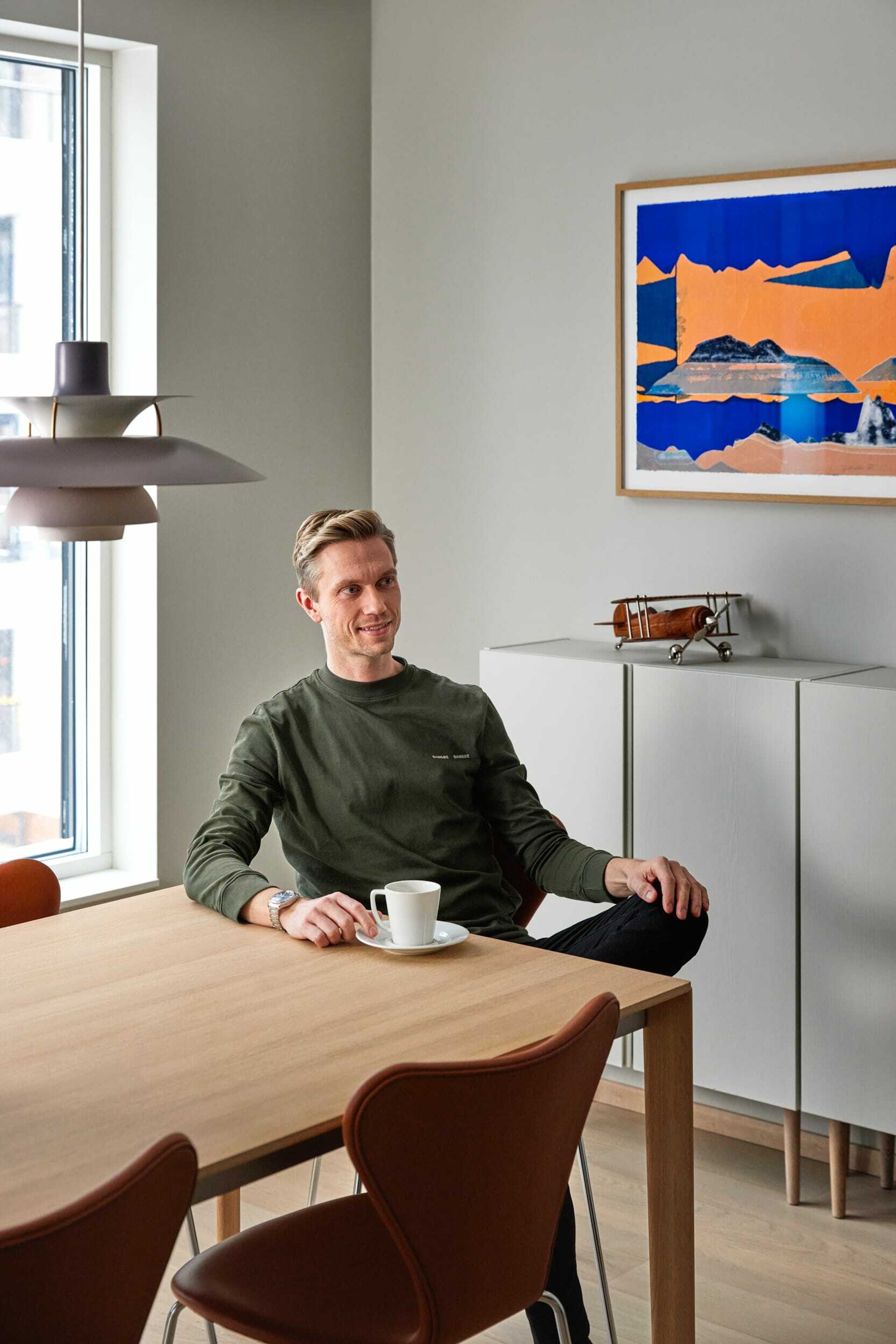Frikk Heide-Steen sitter på stol ved eikefarget spisebord. I bakgrunnen står en hvit skjenk og et fargerikt bilde.