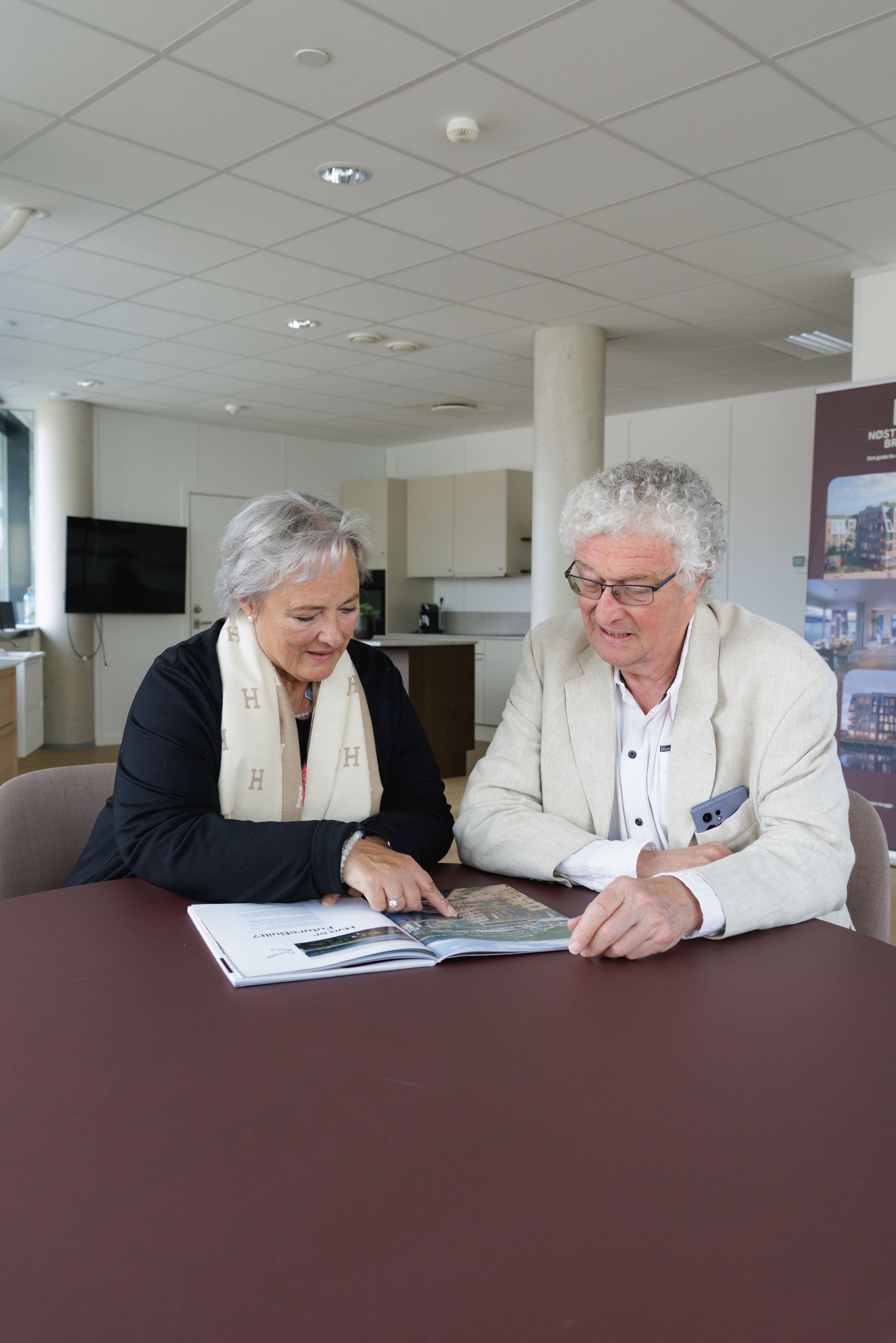Edna og Øyvind sitter ved et burgunder bord og titter i katalogen til Nøstebuktenm Brygge